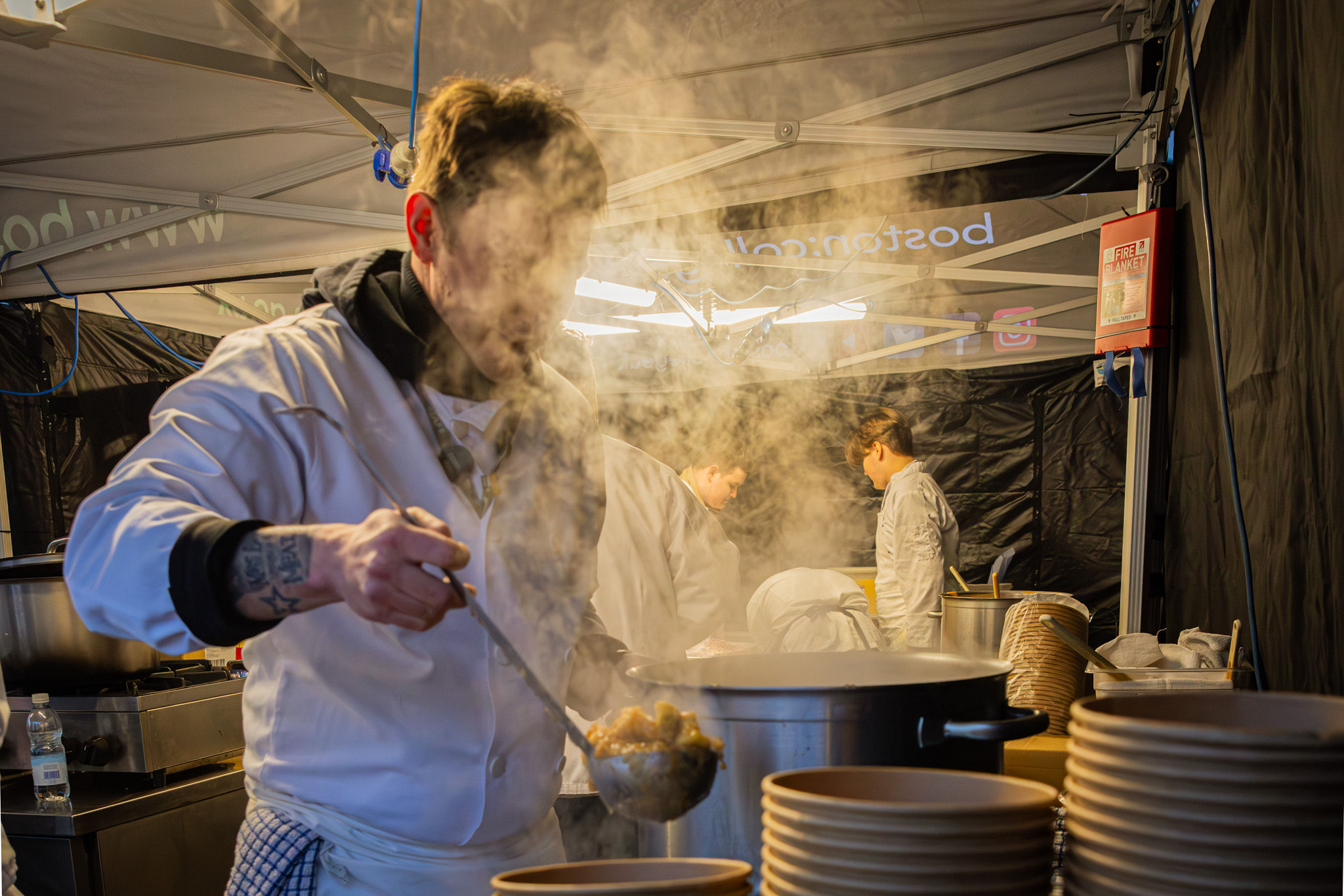 A student chef serving steaming food from a gazebo.