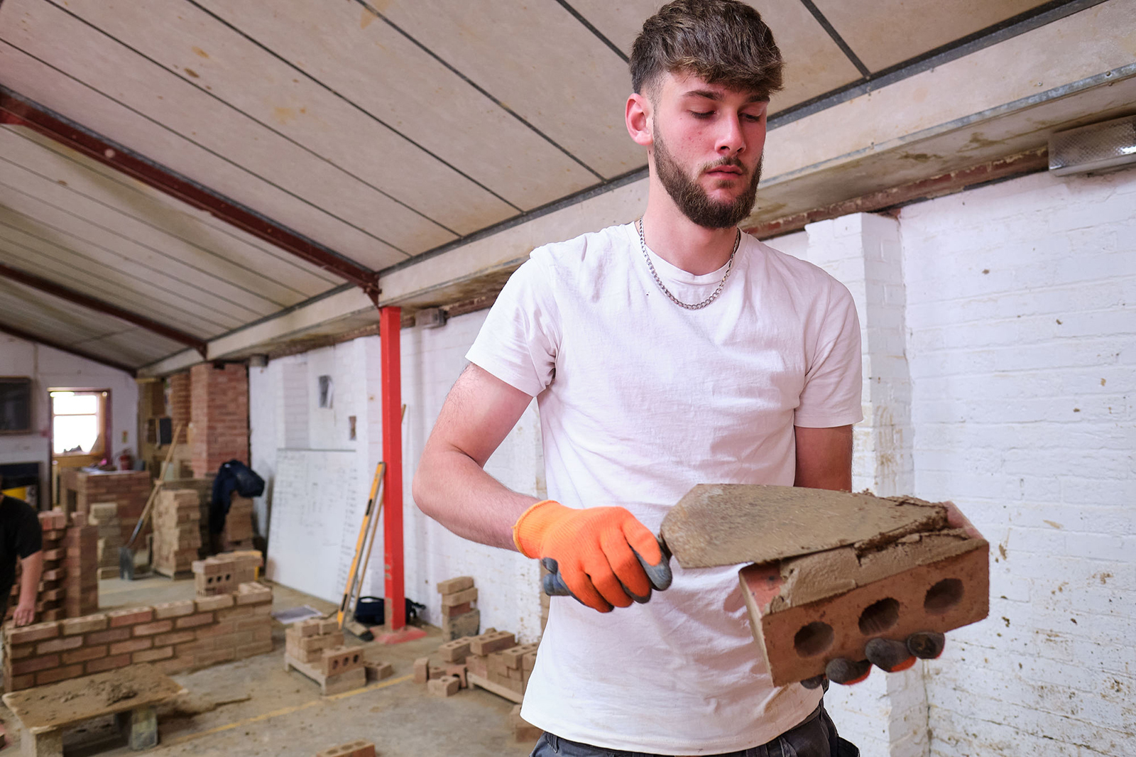 A student placing cement on a brick in the Bricklaying workshop.
