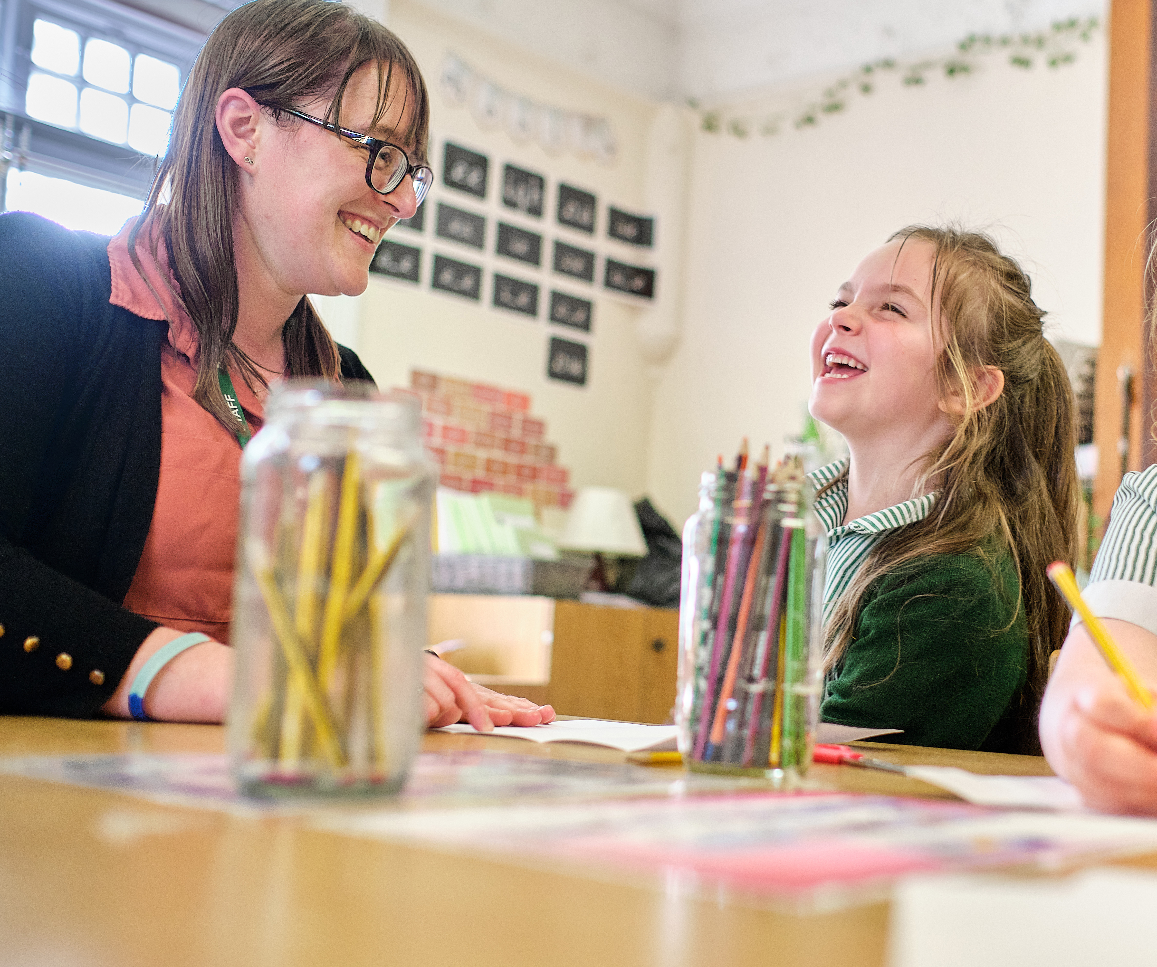 A student sat at a table with a child, laughing and colouring in.