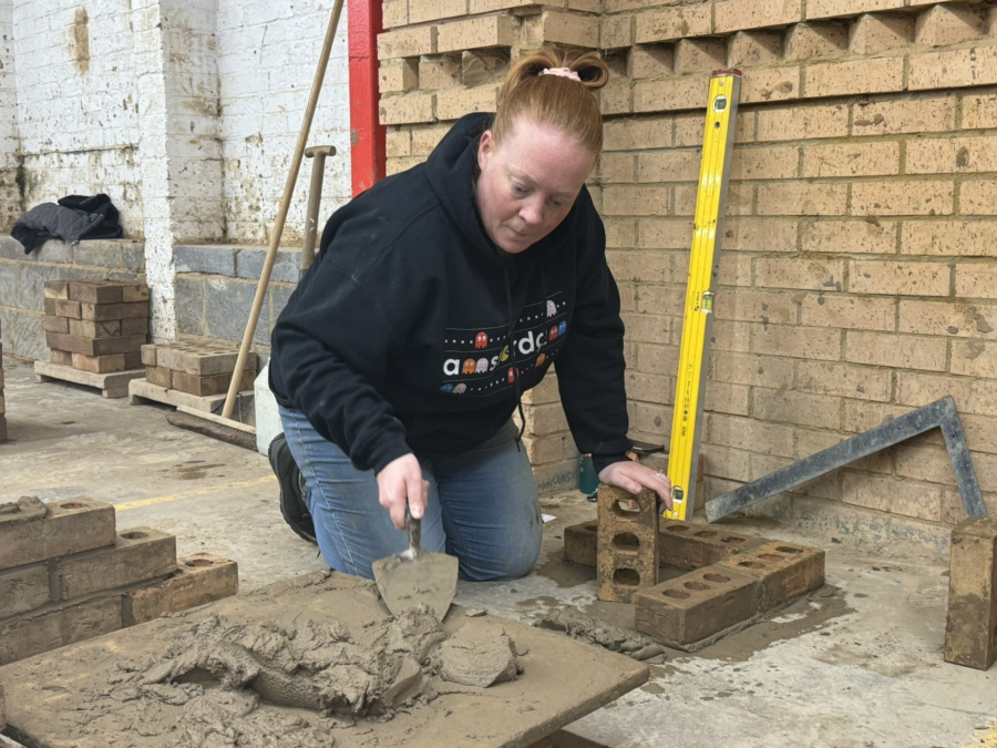 A student mixing cement and building a wall.