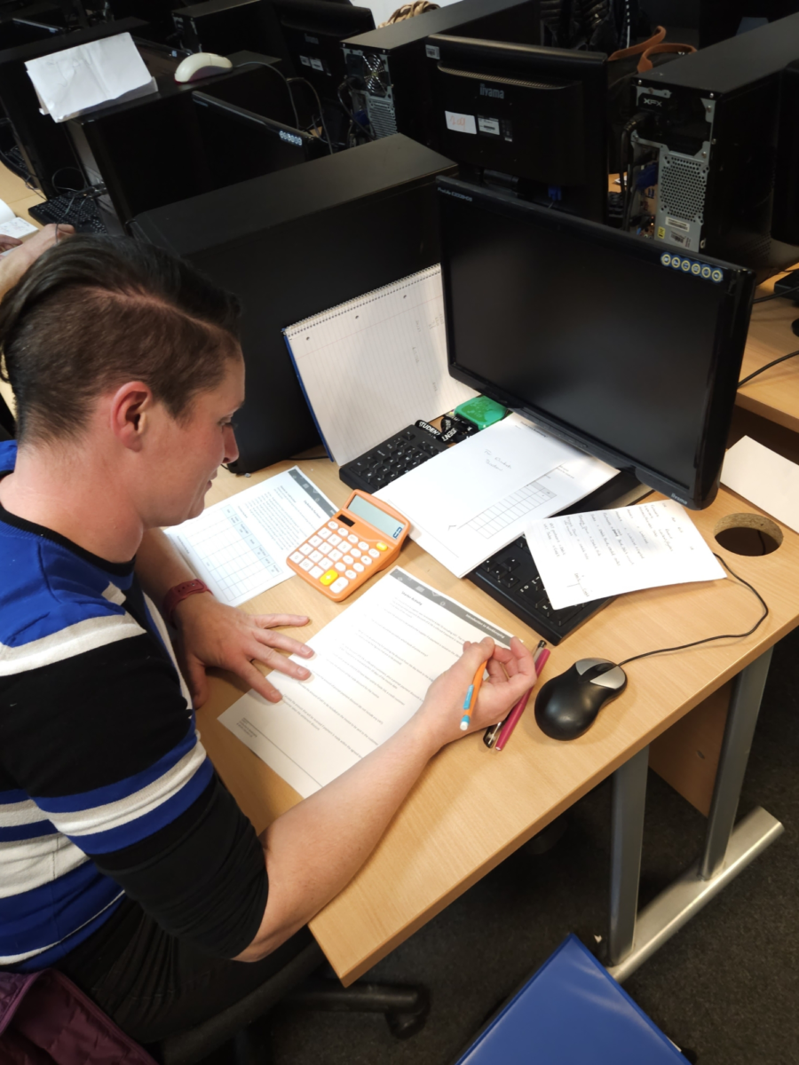 A student sat at a computer writing notes on a worksheet.