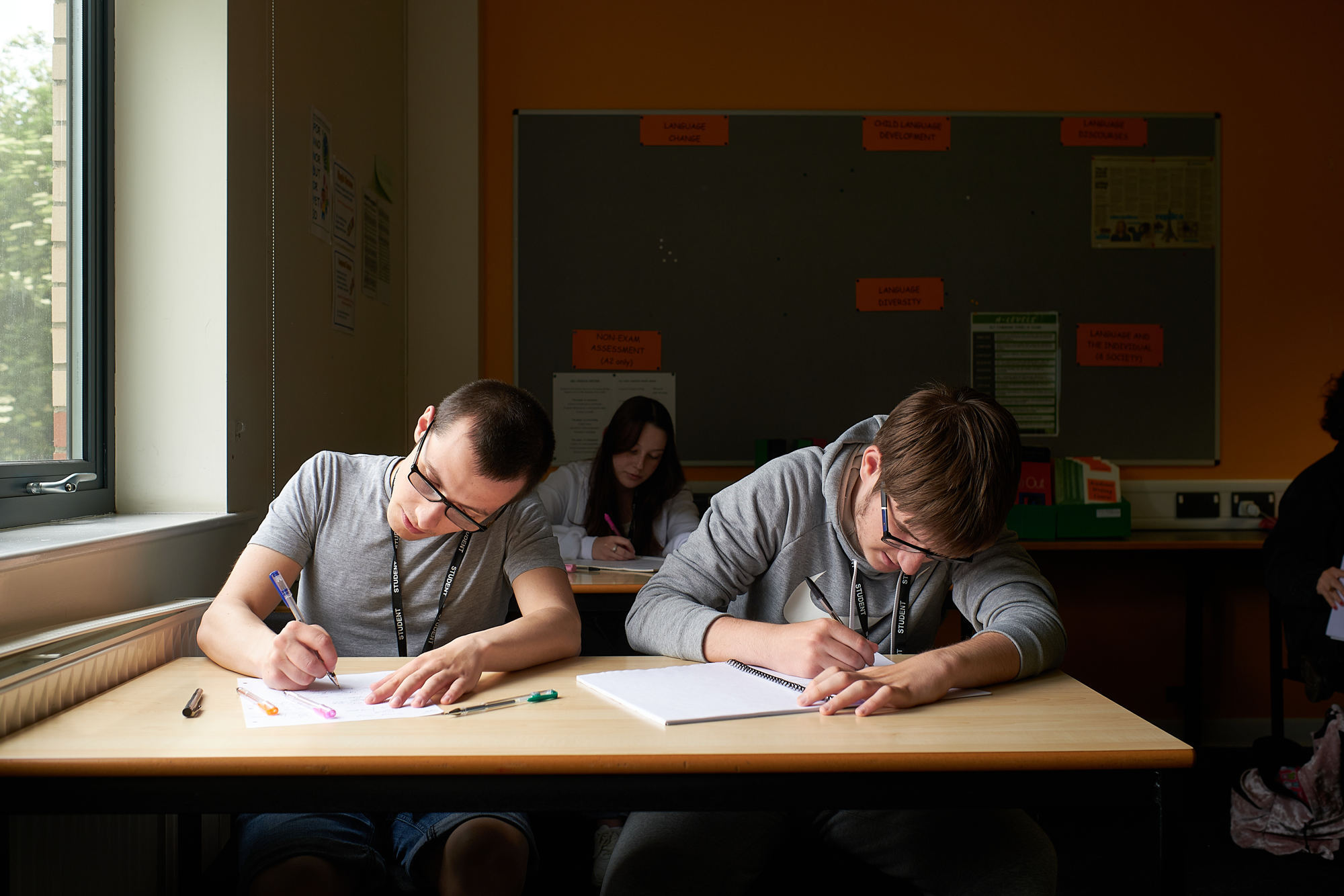 Two students writing notes sat at a classroom table.
