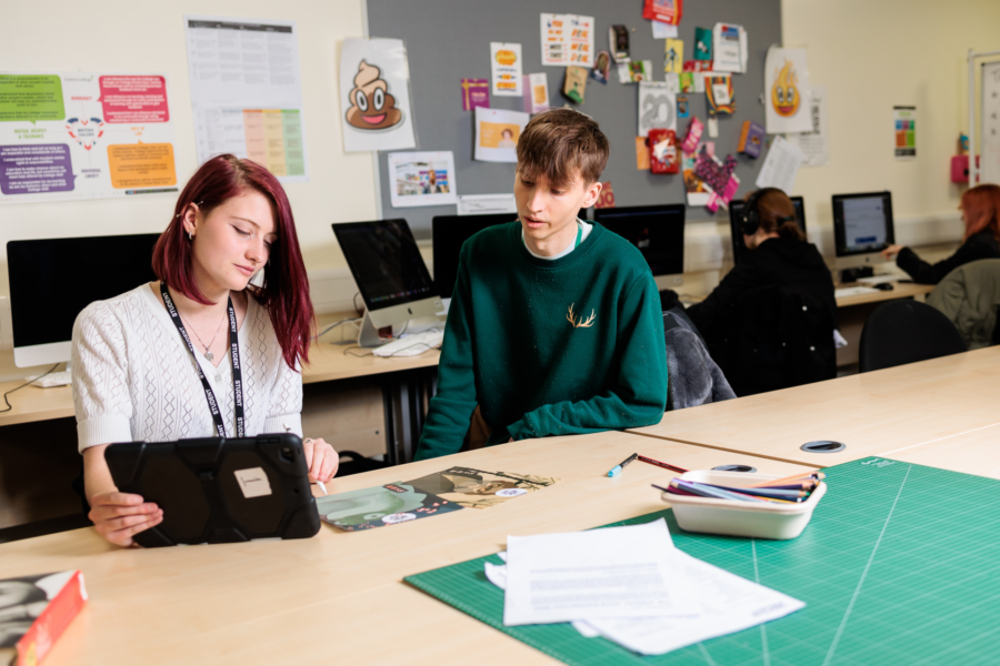 Two students sat at a classroom desk discussing work.