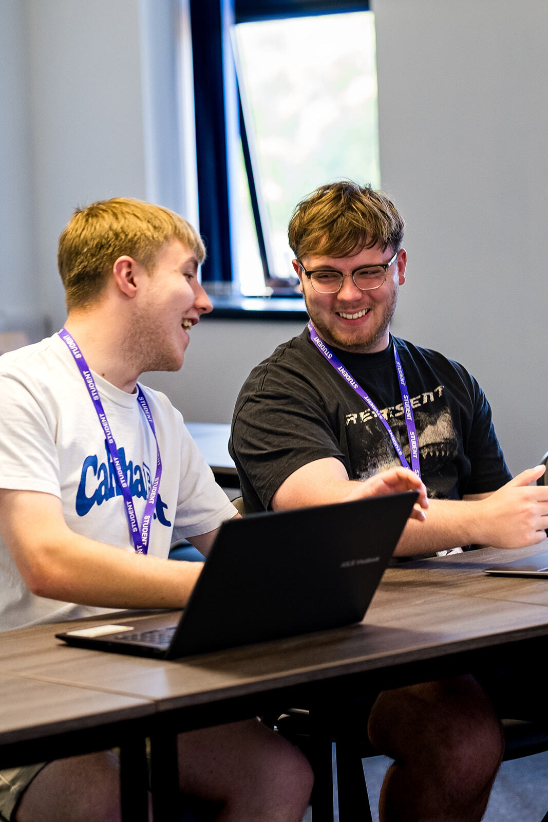 Two students discussing work, sat in front of laptops.