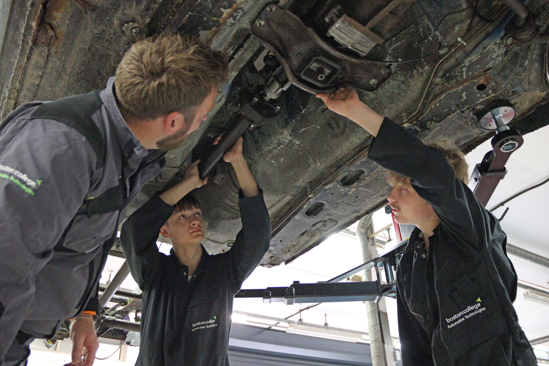 Students and lecturer inspecting the underside of a vehicle.