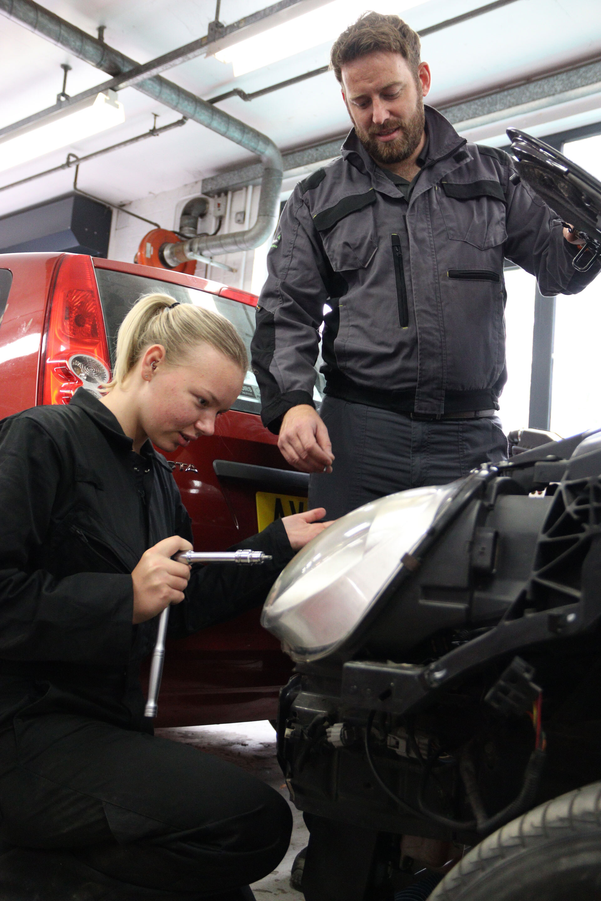 Lecturer supporting a student to change a car headlight.