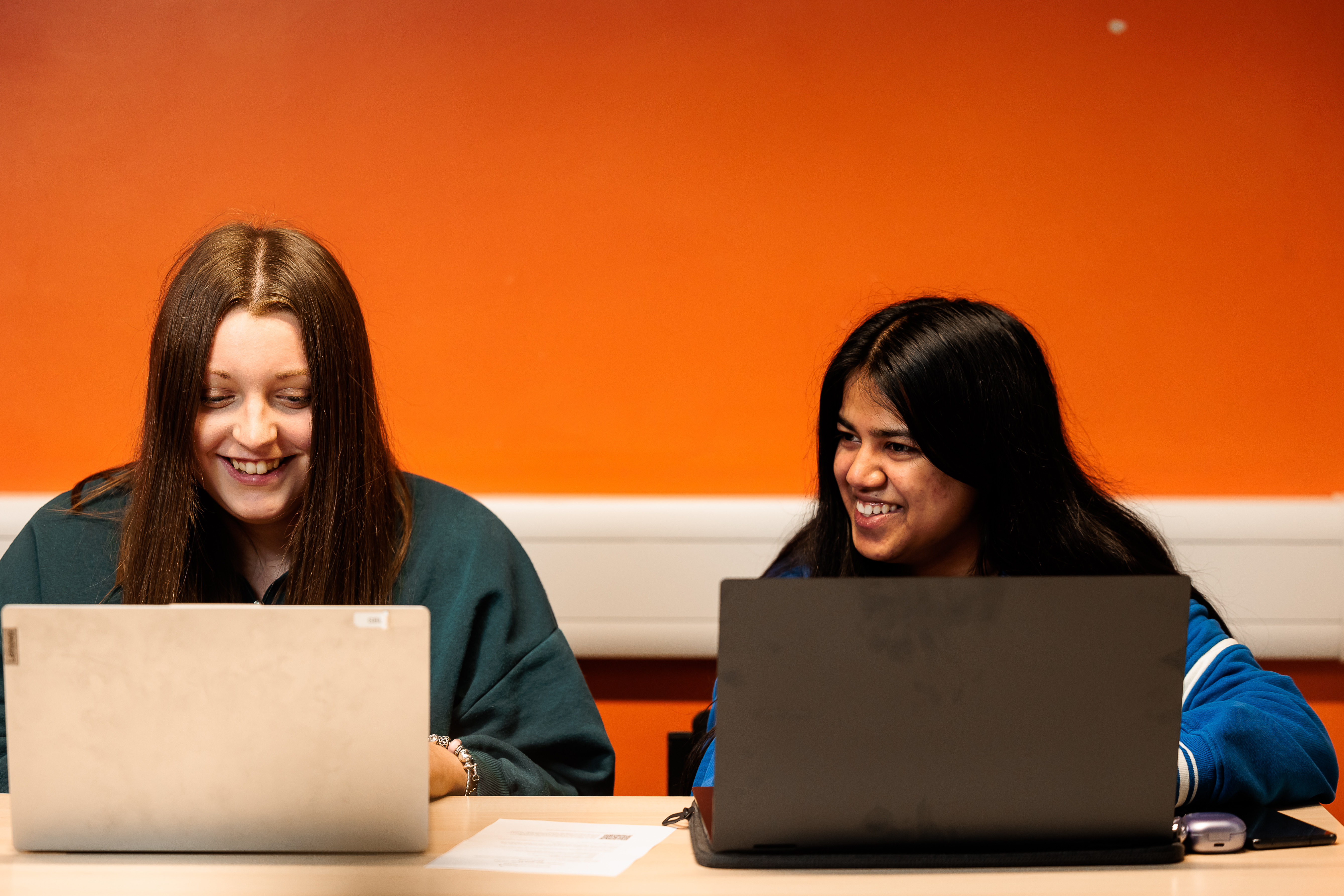 Two students laughing while working on laptops.