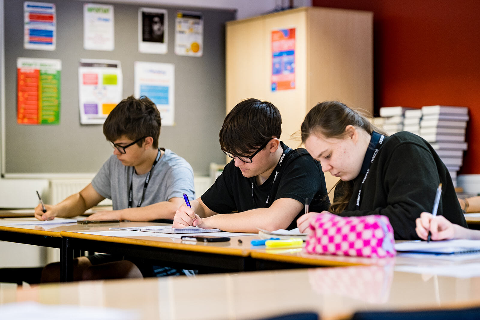 Three students writing notes in a classroom.