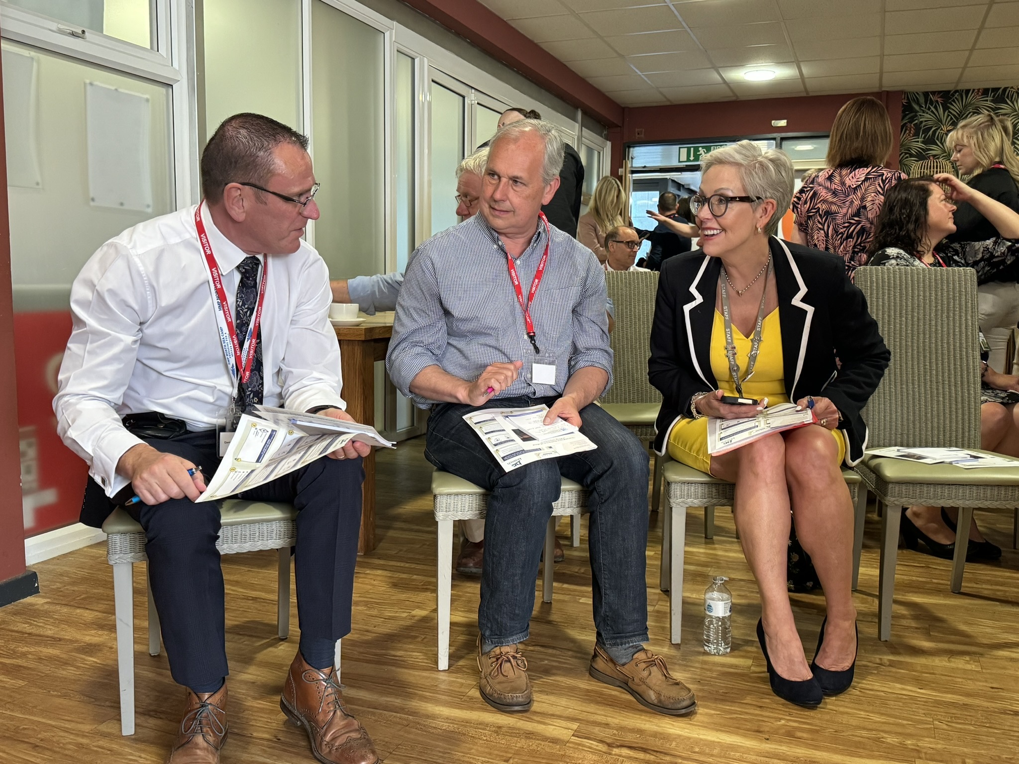 Three people with paperwork and notebooks having a discussion.