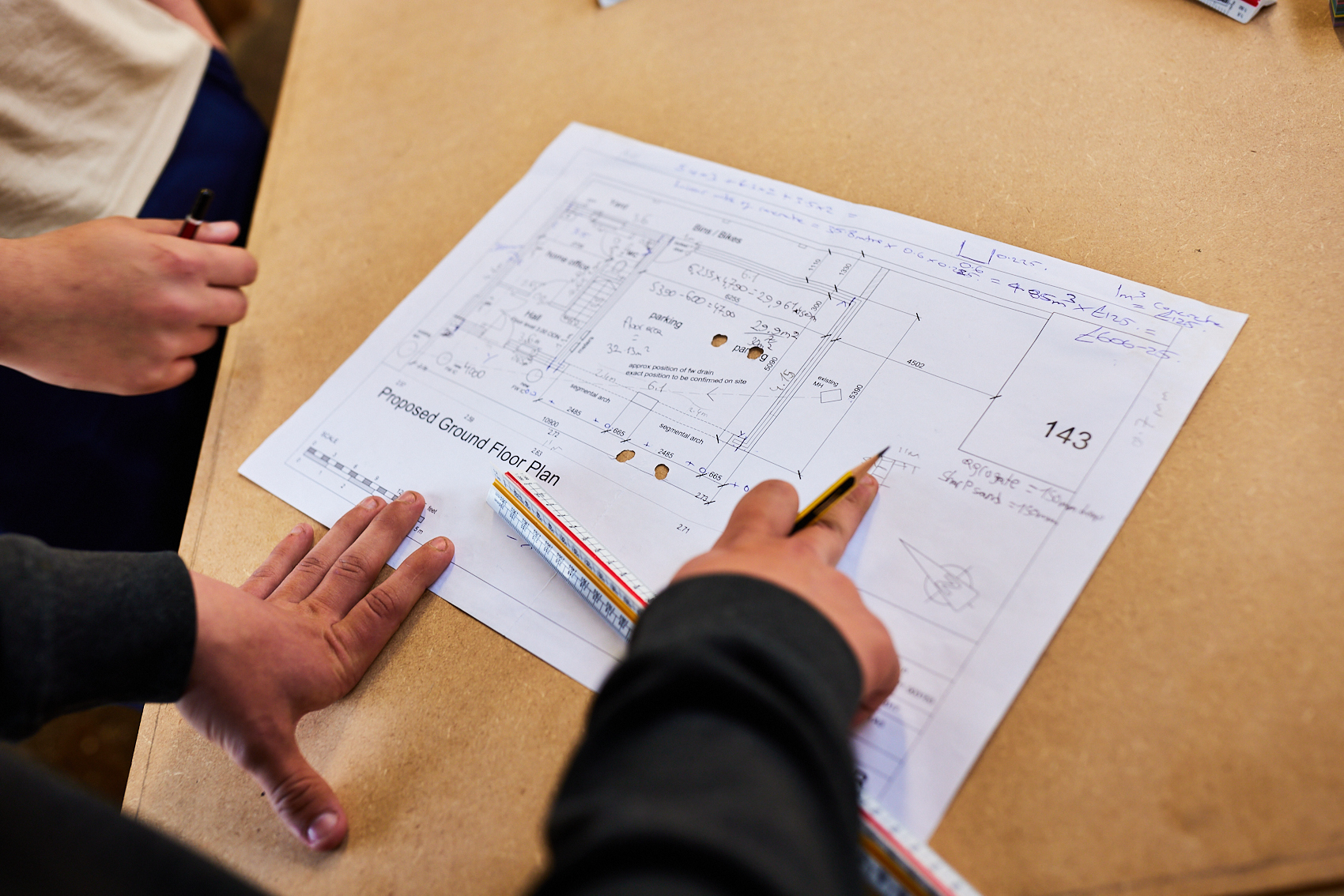 People looking and pointing at plans on a desk.