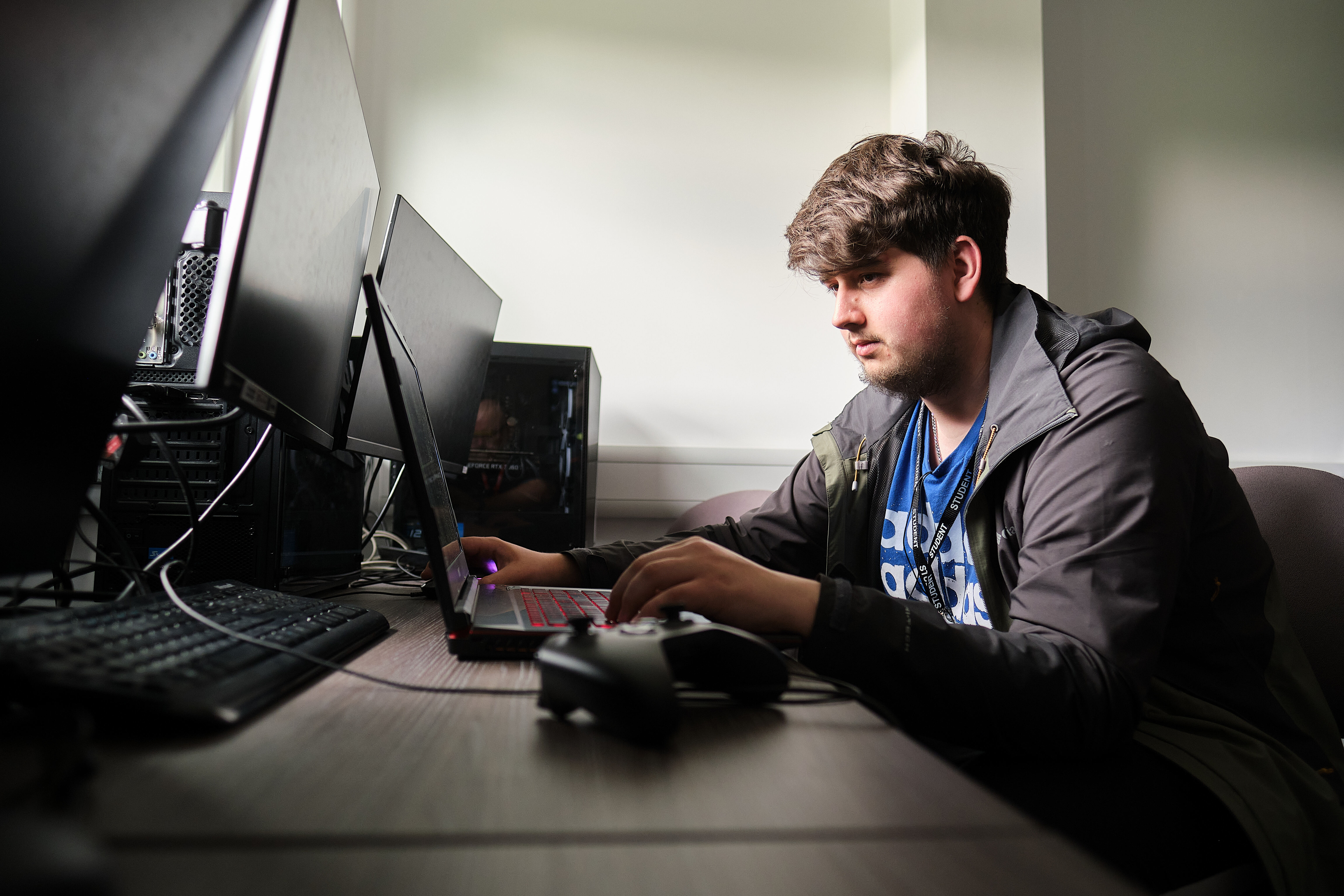 A student sitting at a selection of computer screens and typing on a laptop.