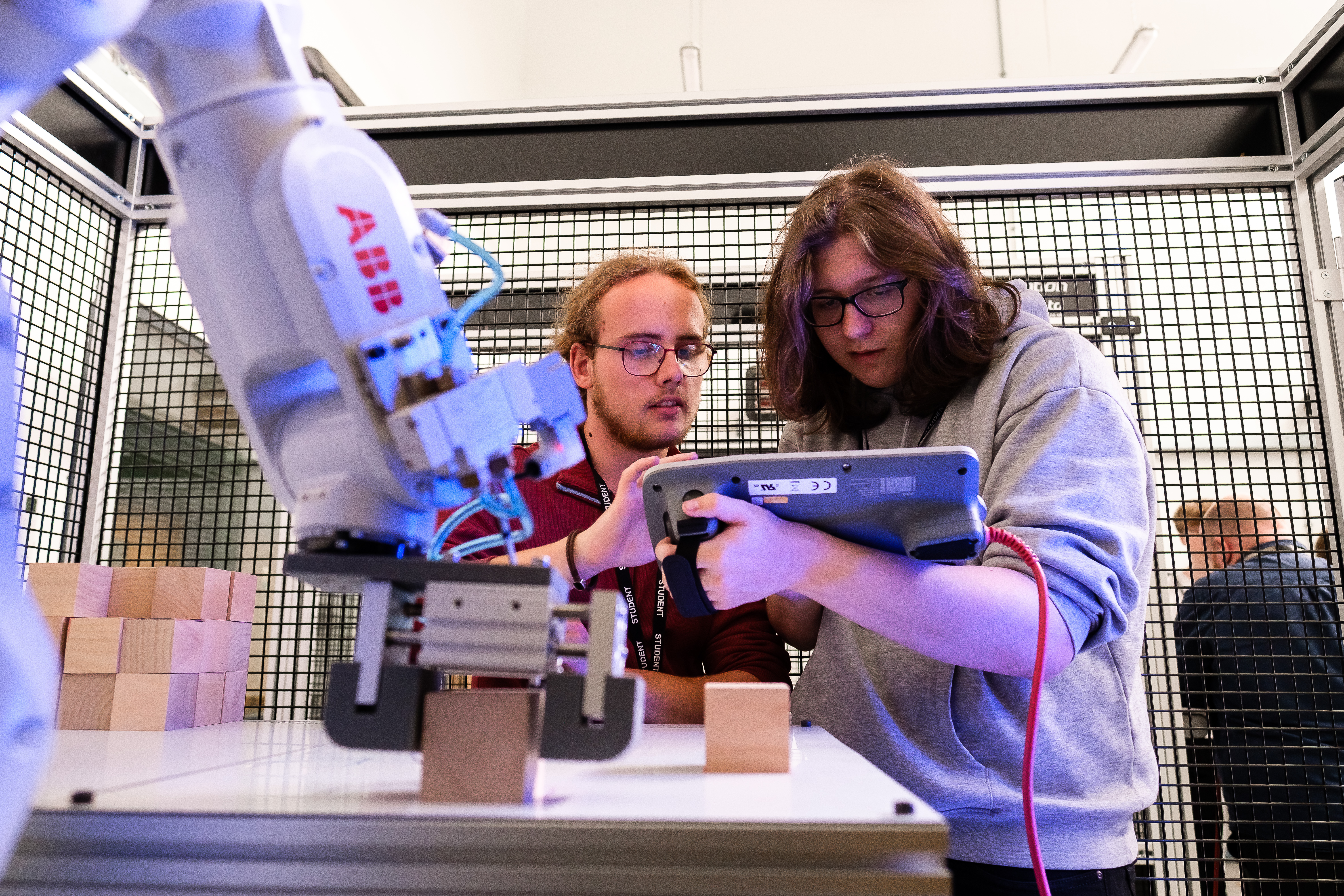 Two students looking at a tablet while working on robotic machinery.
