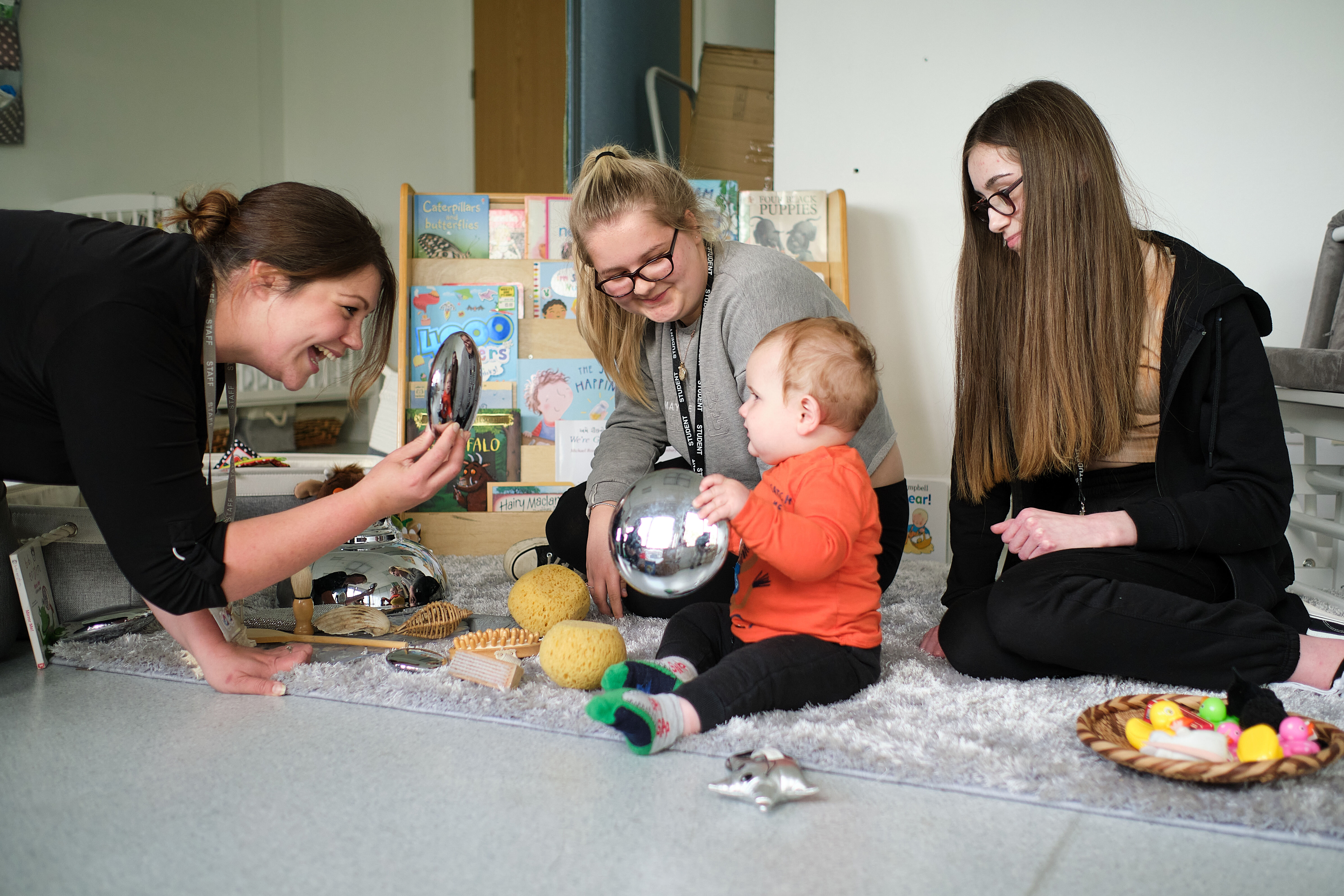 Three students sat with a toddler playing with toys.