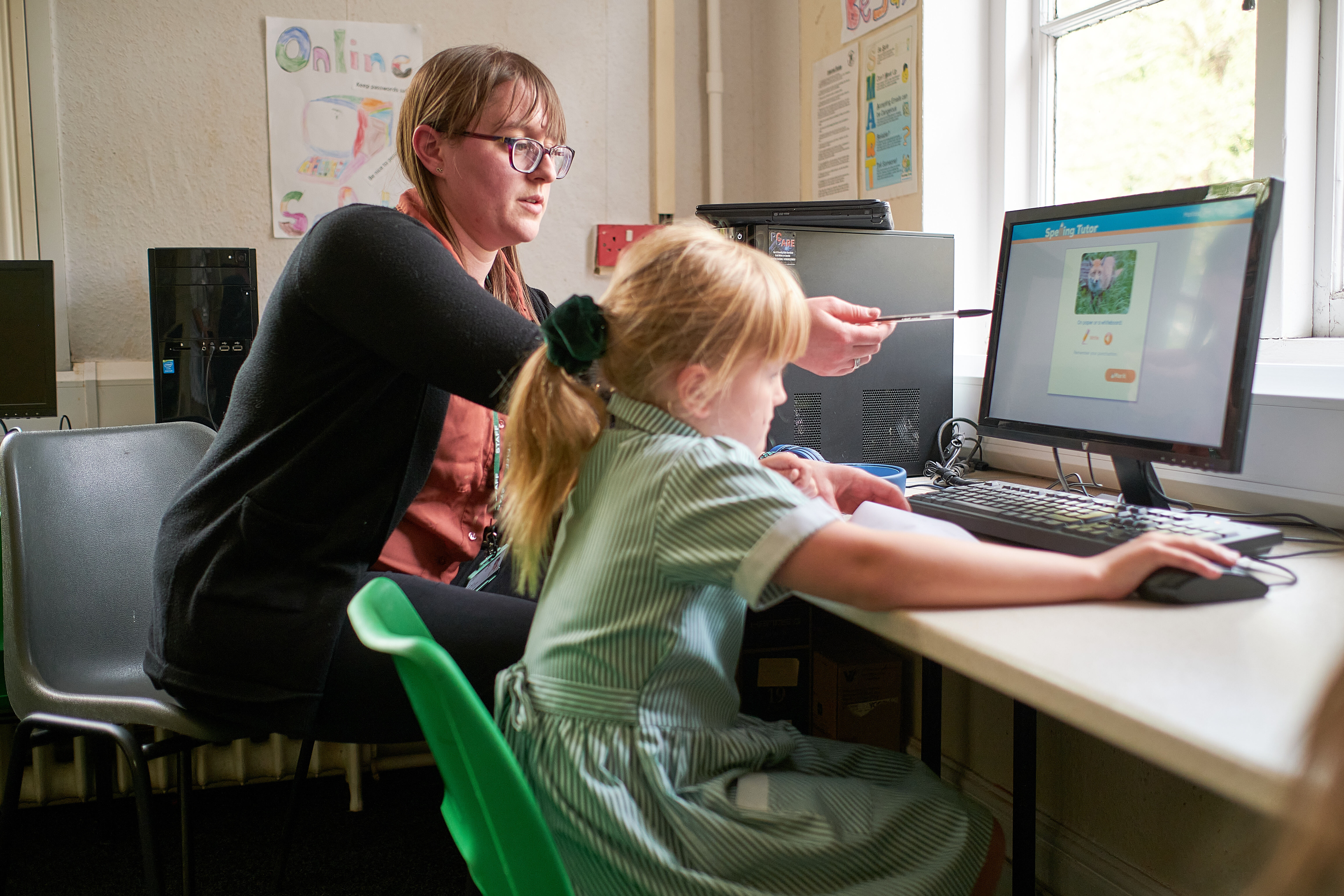 A person points to an item on a computer screen as a child uses the computer mouse.