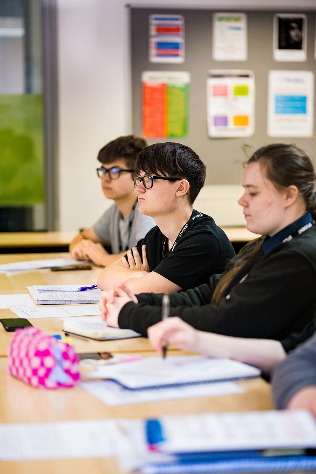 A group of students sitting at desks listening to a lesson.