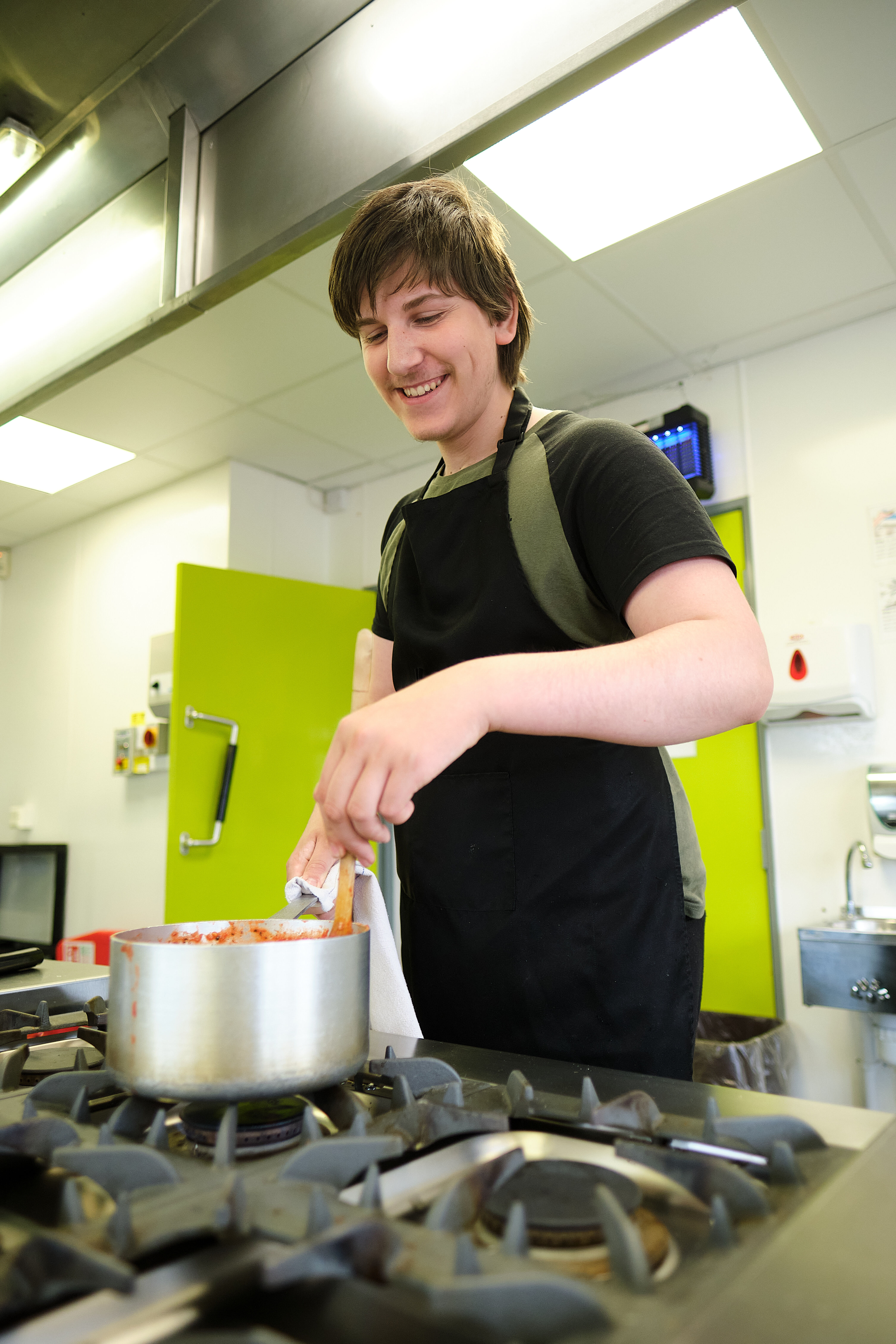 A student cooking and stirring food up in saucepan.