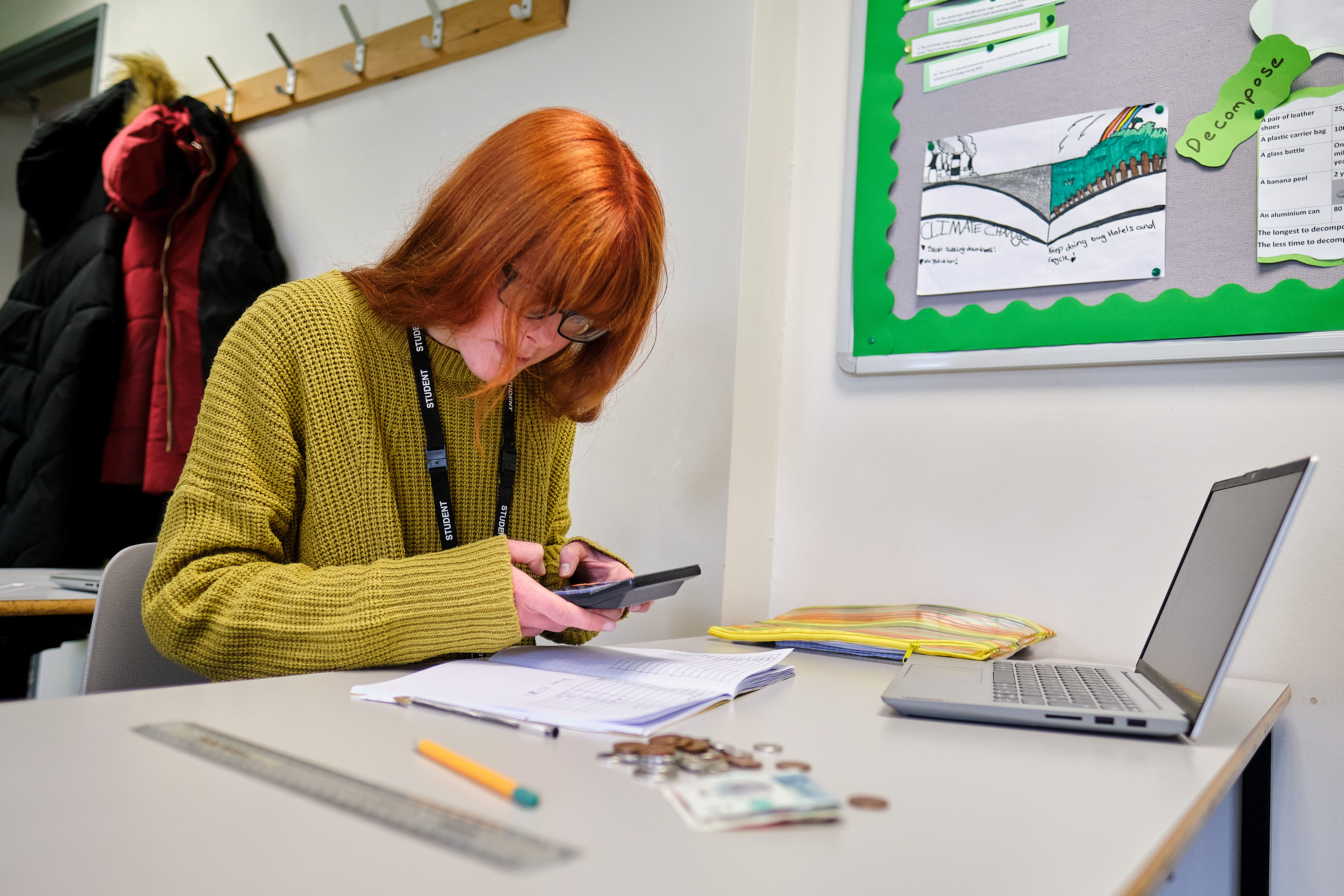 A student using a calculator with coursework sat on the table in front of them.