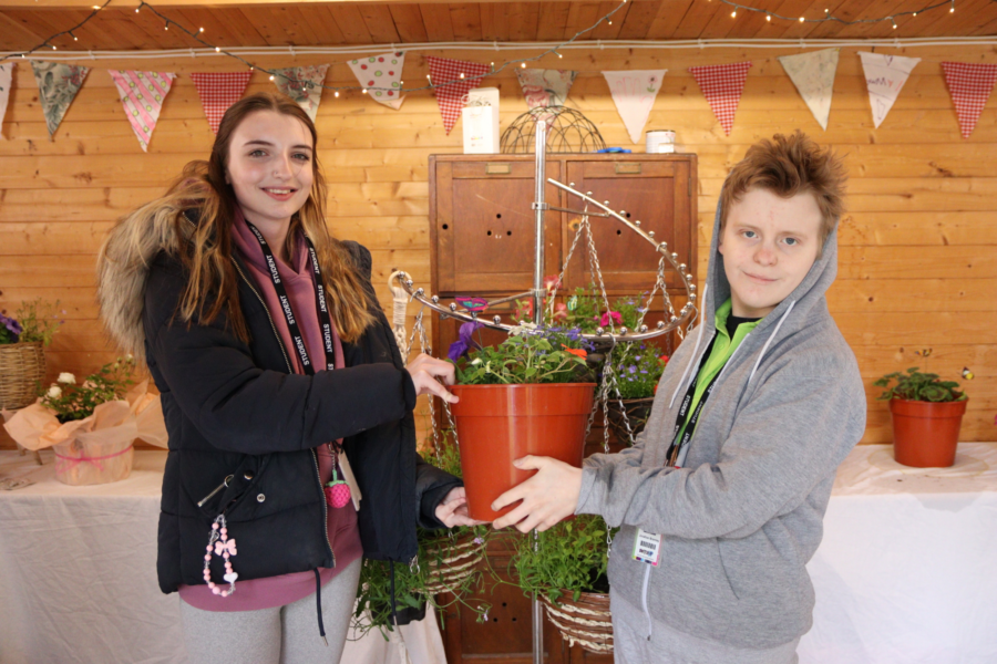 Two students hold a potted plant in a summer house.