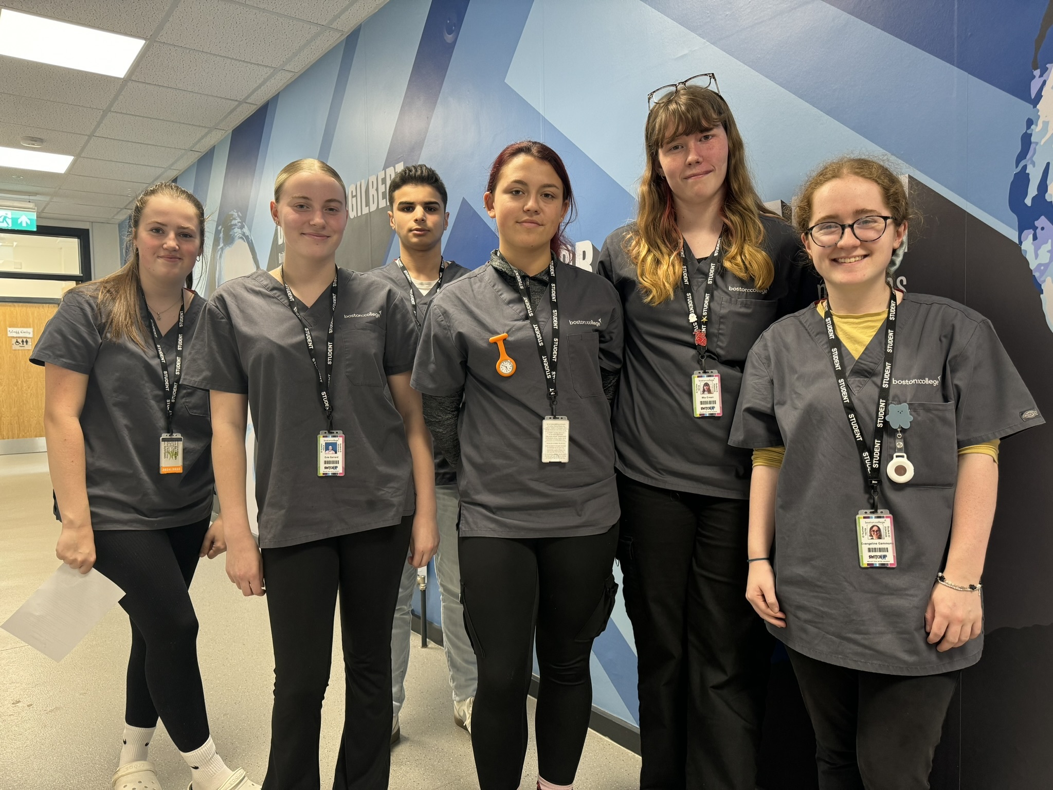 A group of six Boston College Health & Social Car learners showing off their new uniform in the Care Core corridor.