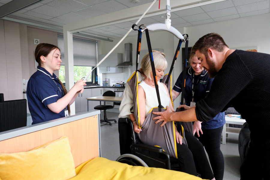 A group of students helping lift a patient into bed via a hoist.