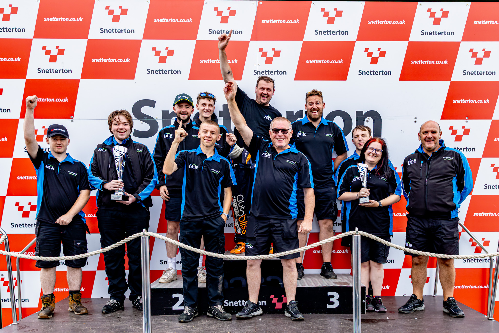 Boston College Racing team posing with a trophy on the podium.