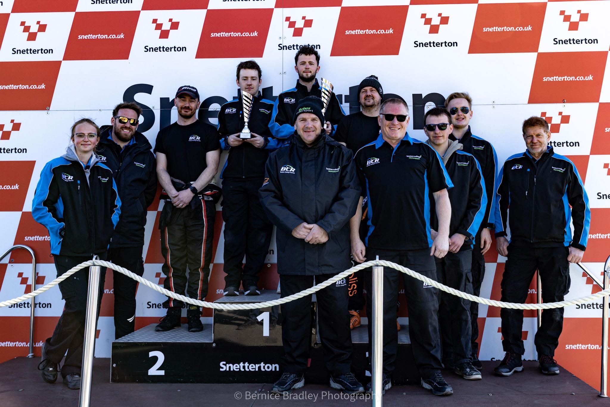 Boston College Racing team posing with a trophy on the podium.