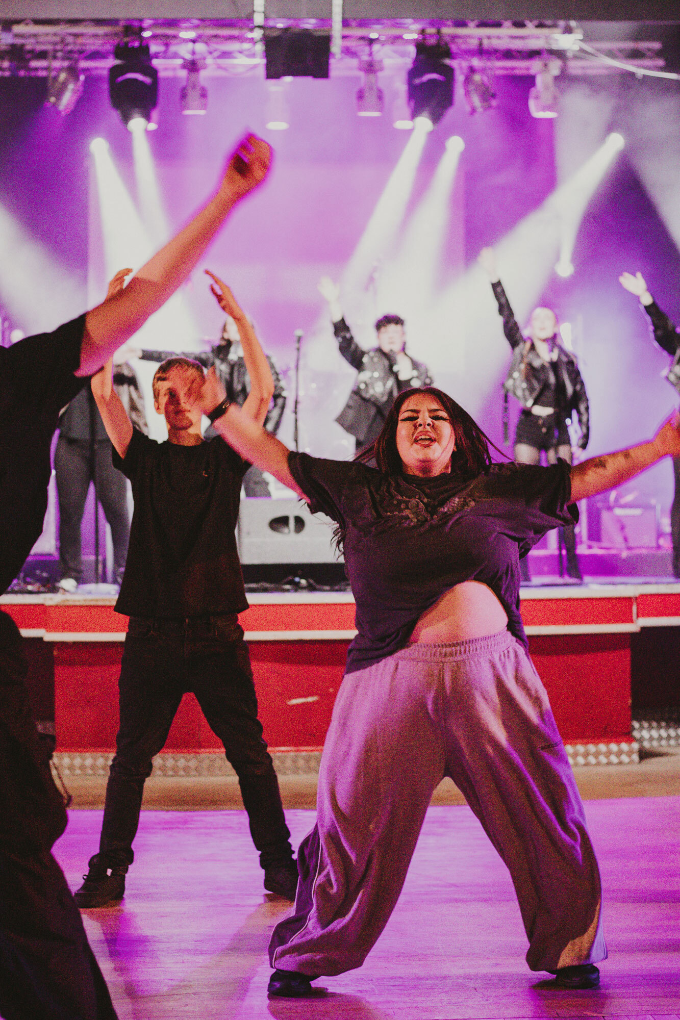 A student dancer performing on a dancefloor with a student band on the stage behind.