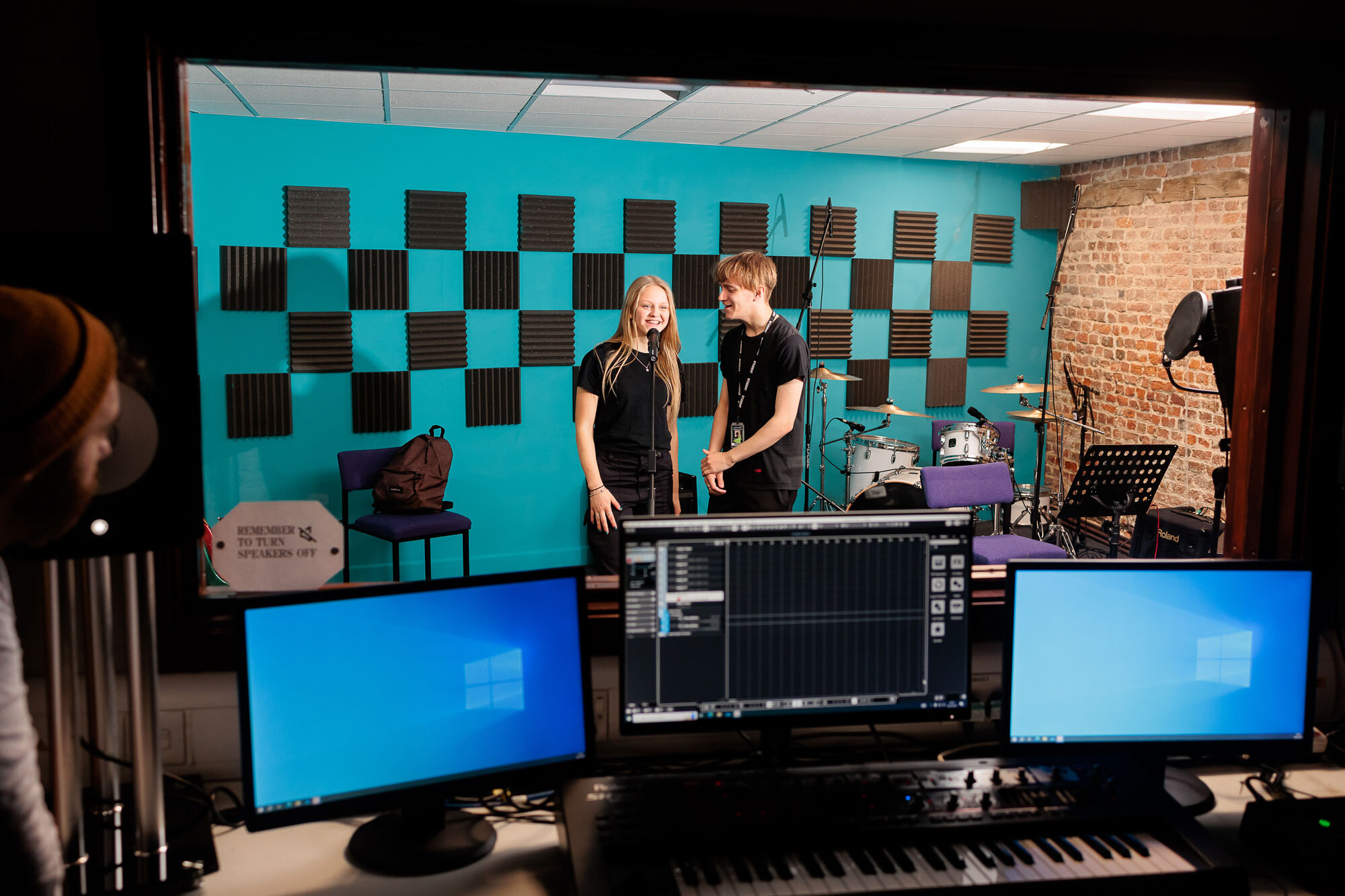 Two students singing in a recording studio with recording equipment in the foreground.