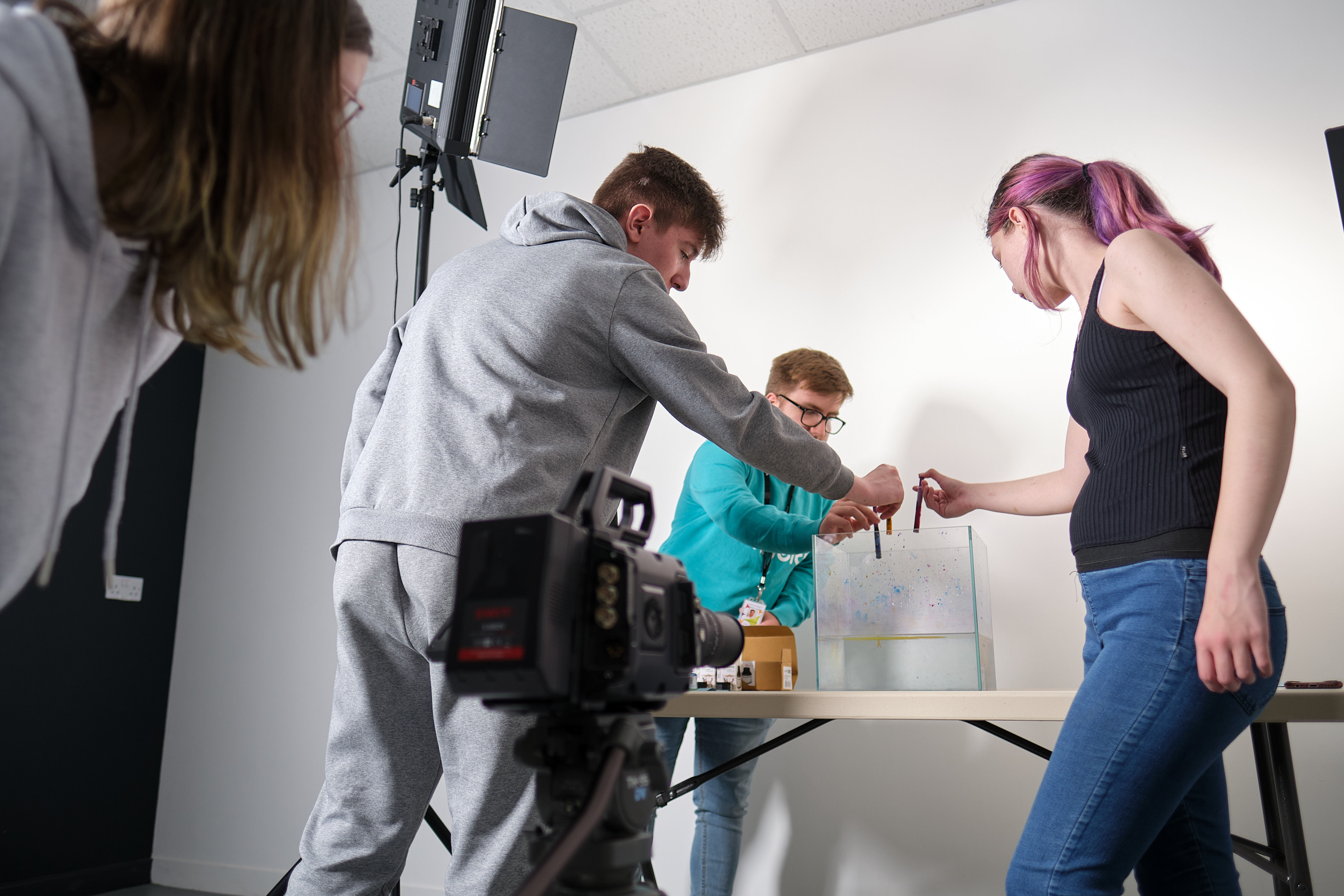 A group of students setting up a shot in the background as another student looks through a camera.