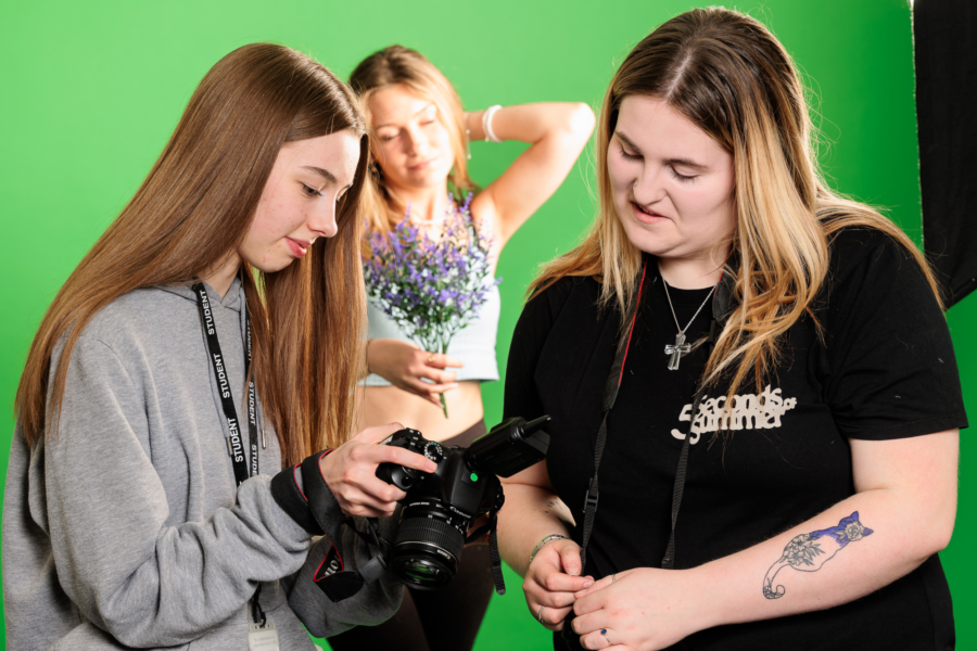 Two students discussing a photograph on a camera with the subject stood against a greenscreen in the background.