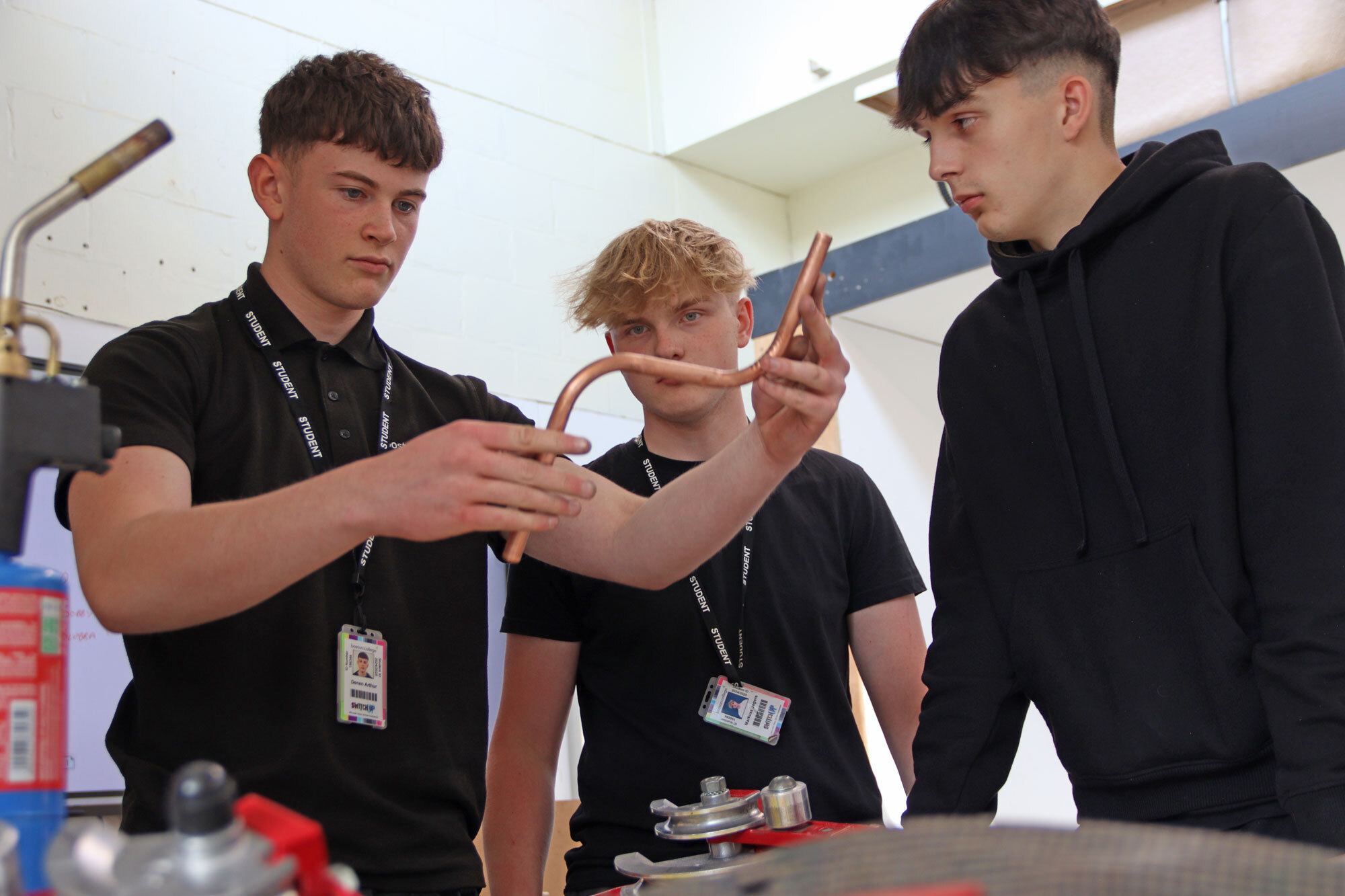 Three students looking at copper piping in the Plumbing workshop.
