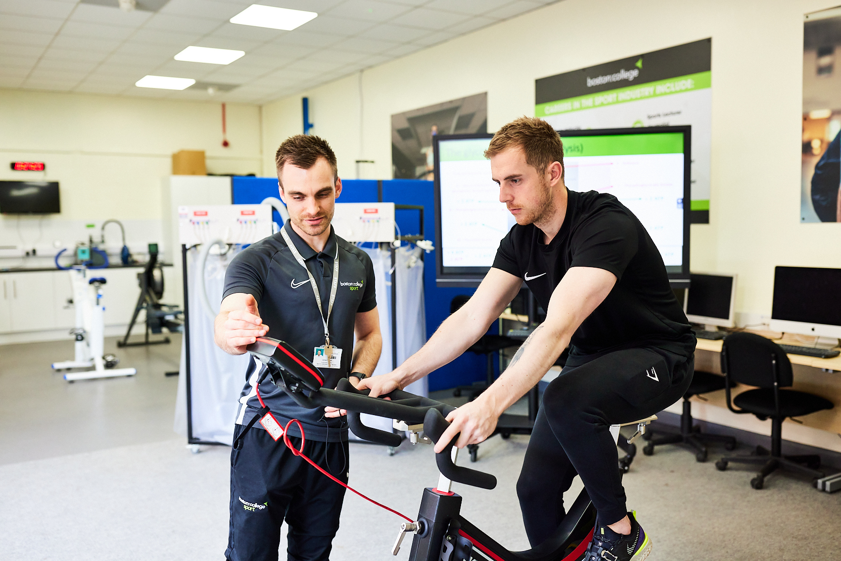A lecturer reviews stats from a student working an exercise bike.