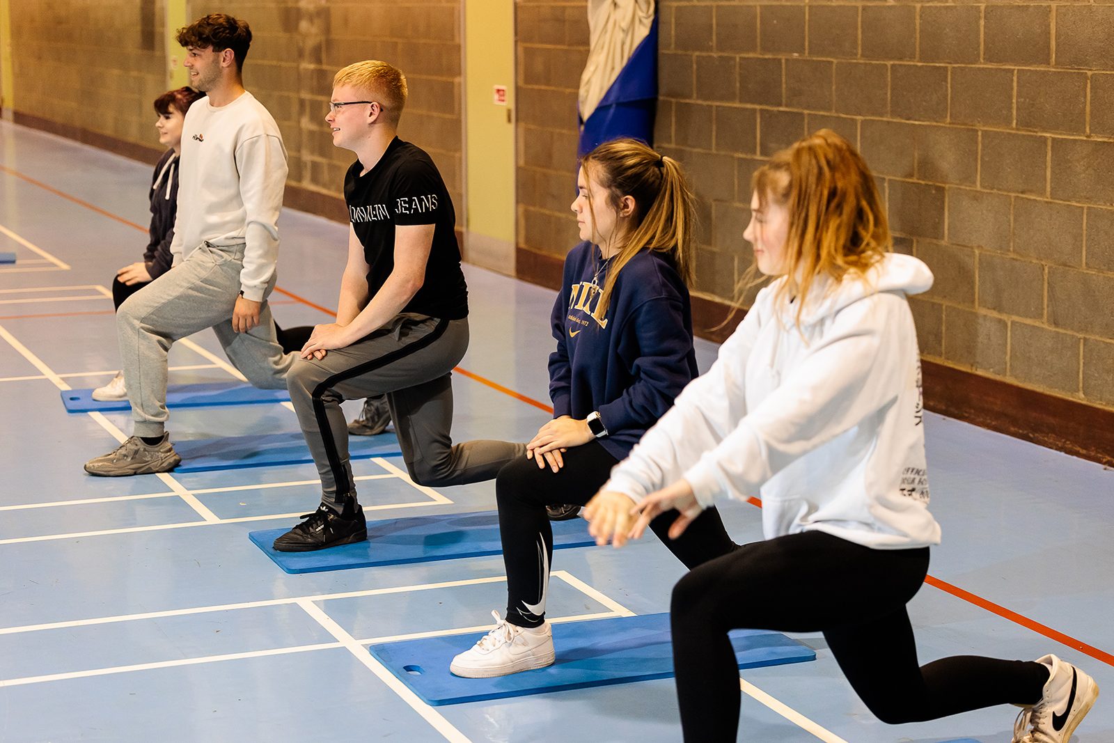 Students lined up performing stretches in a sports hall.