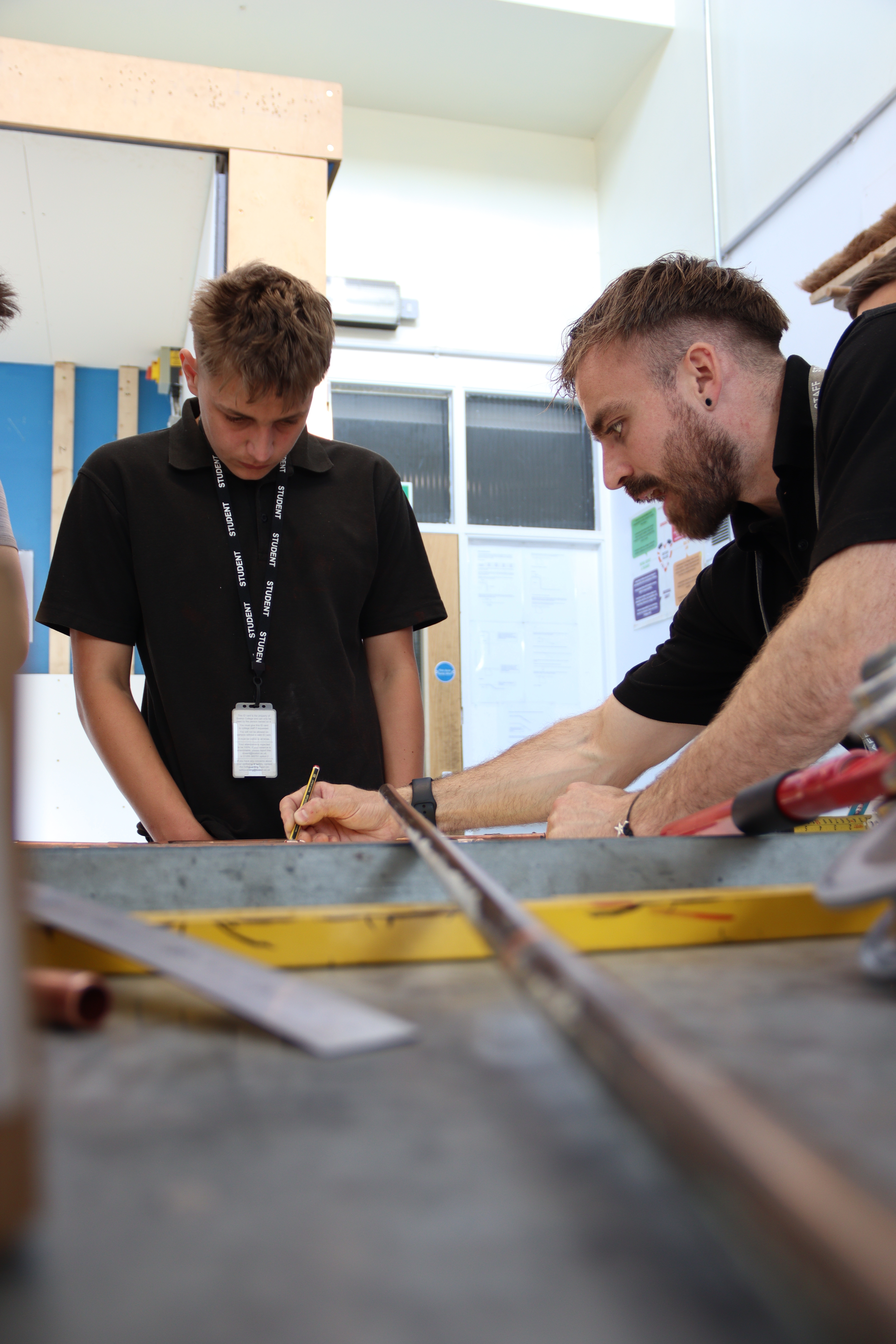 A lecturer supports a student to cut copper piping in the plumbing workshop.