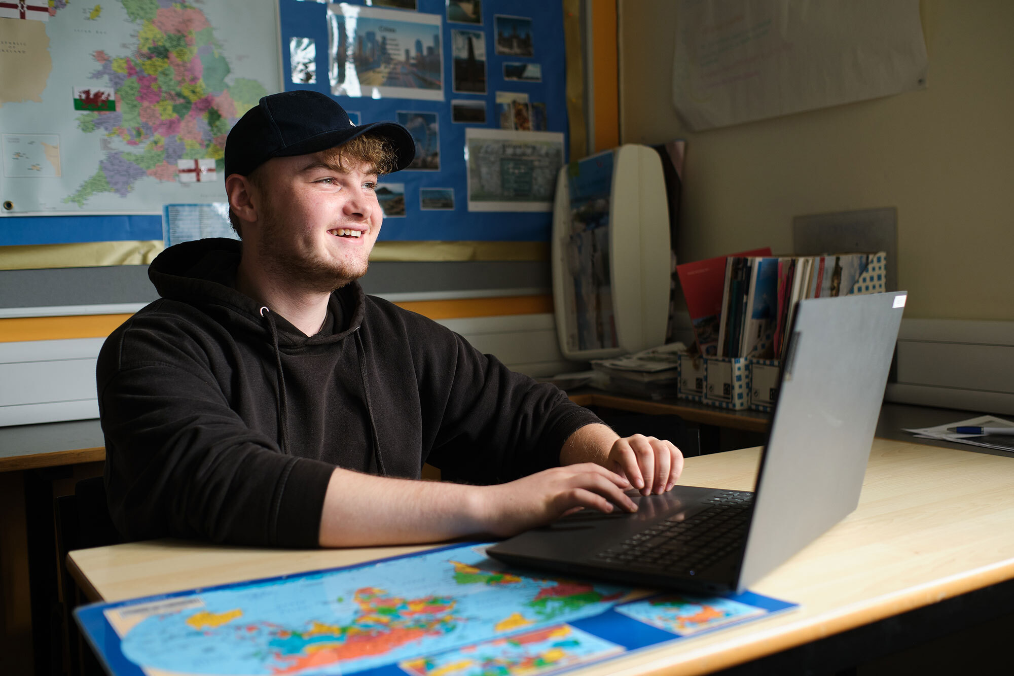 A student looking up from their laptop and map on the desk.