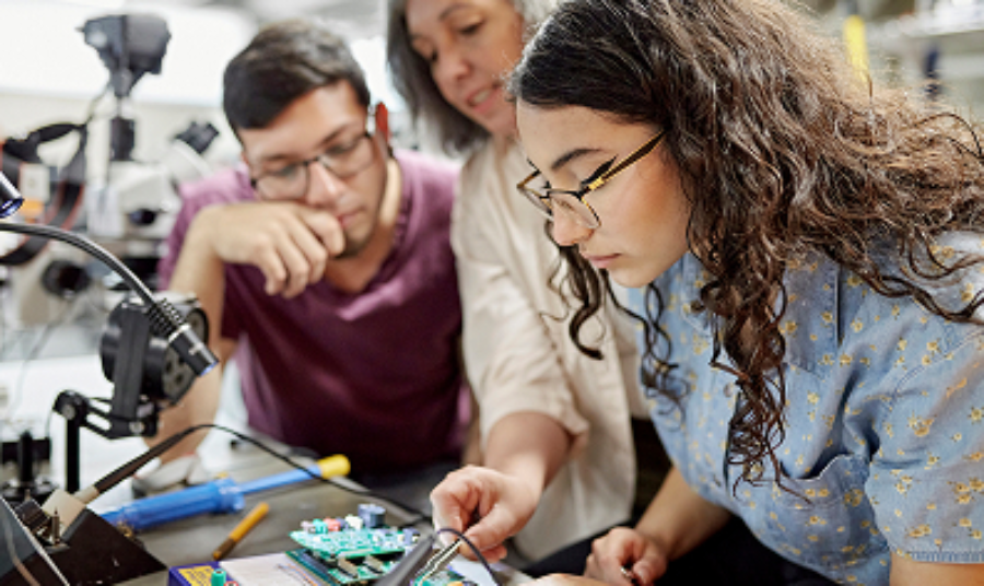 A lecturer shows two students how to use some machinery in a workshop.