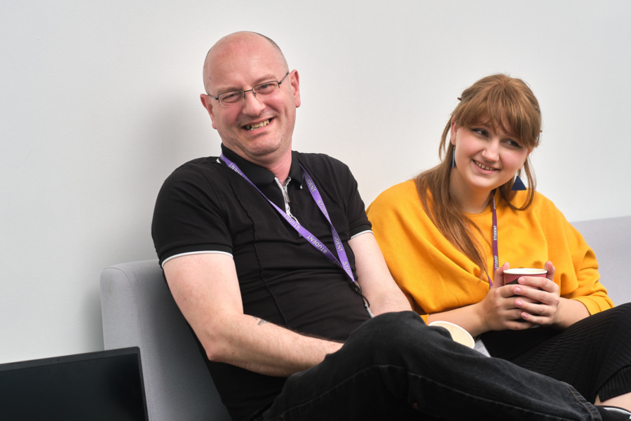 Two adult learners laughing and joking while sat down.