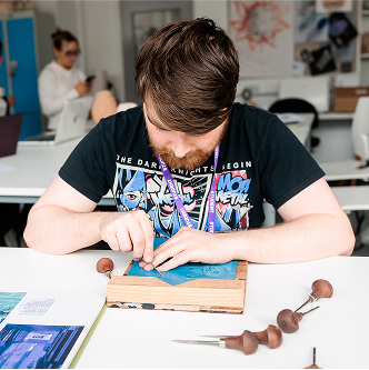 An art student using tools to carve out wood.