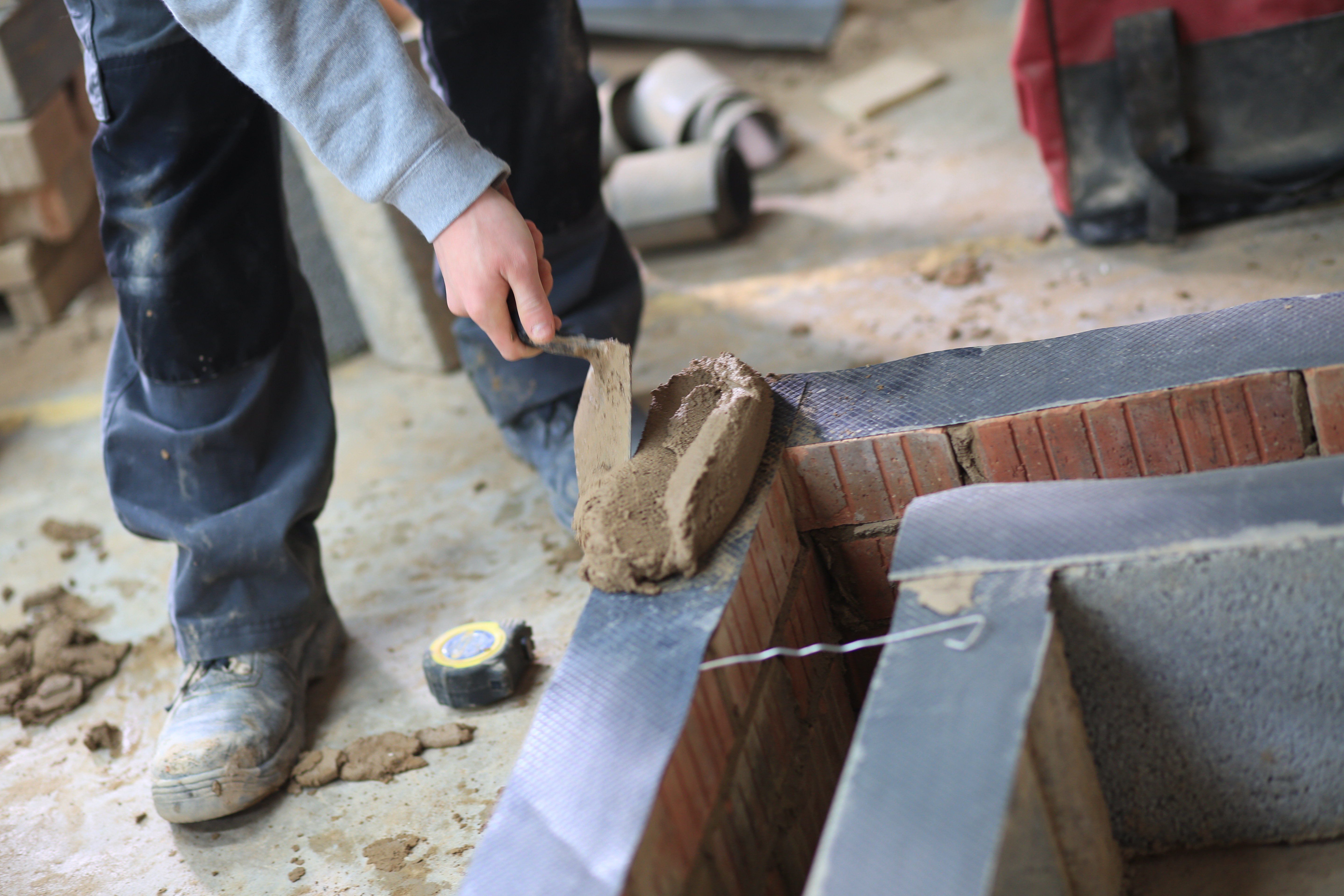 A person laying cement on a brick wall.