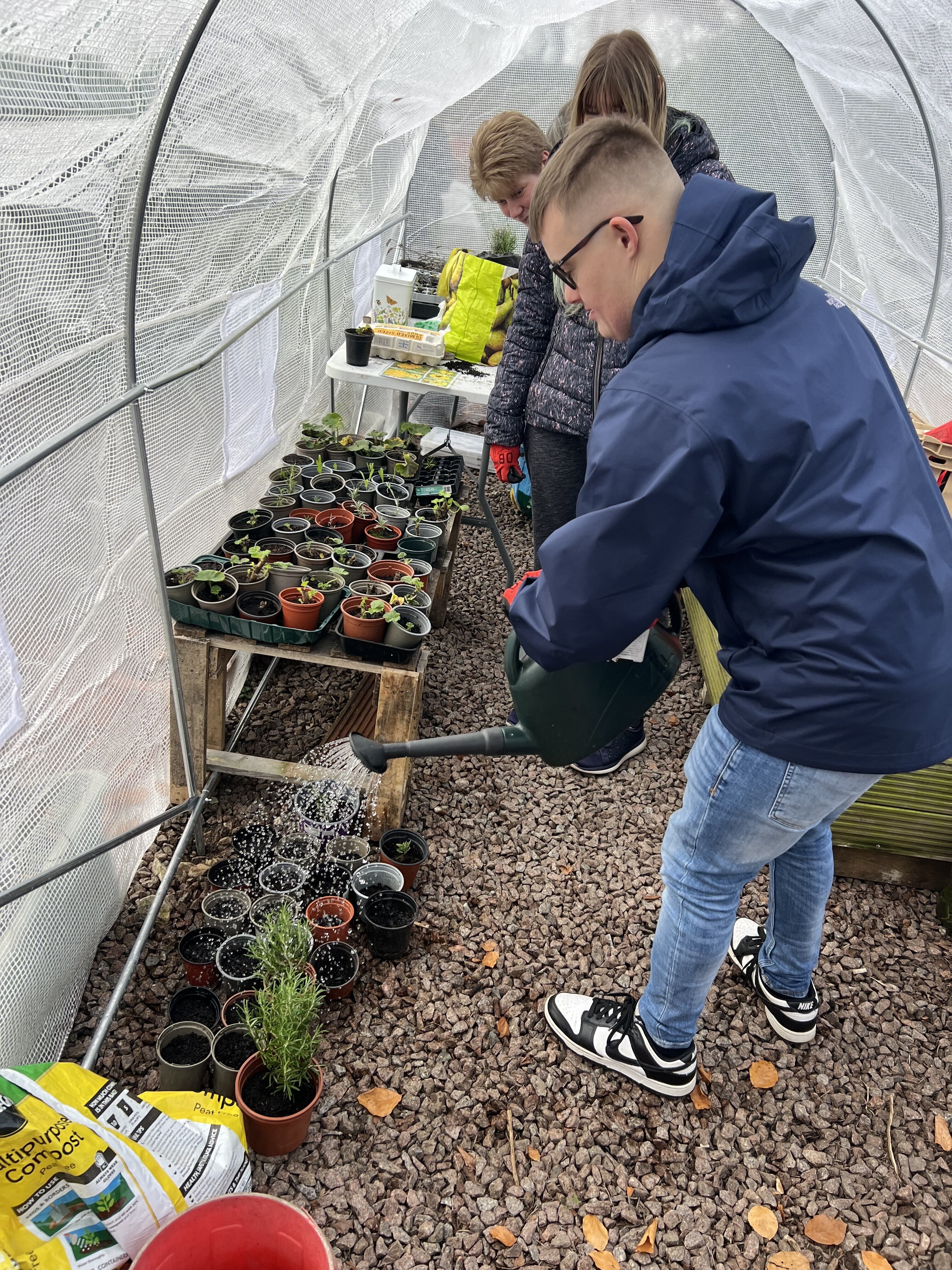 A student watering a plant with a watering can.