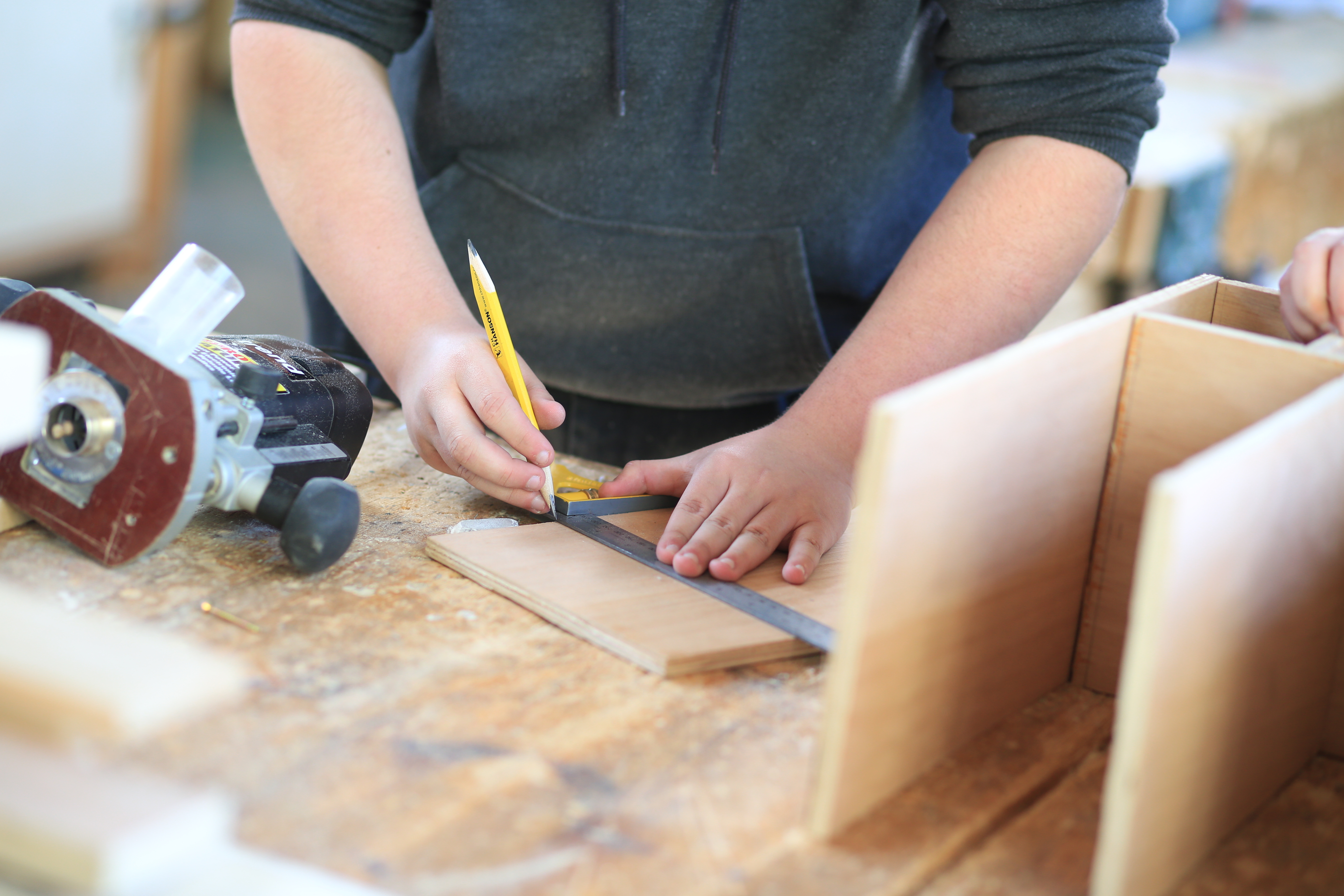 A student measuring a piece of wood and drawing a guide with a pencil.