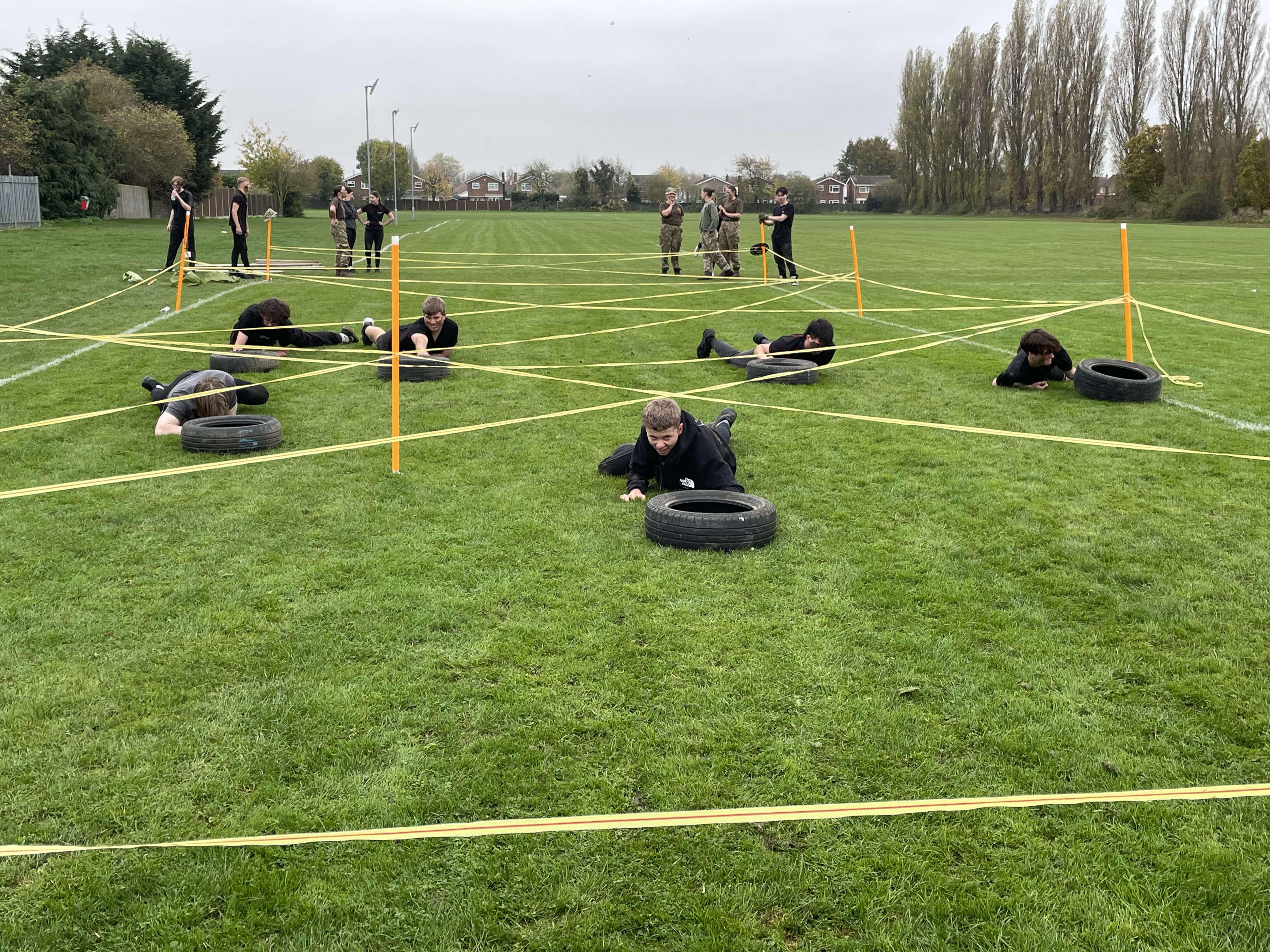 Uniformed Public Service students crawling underneath a wire assault course on a green field.