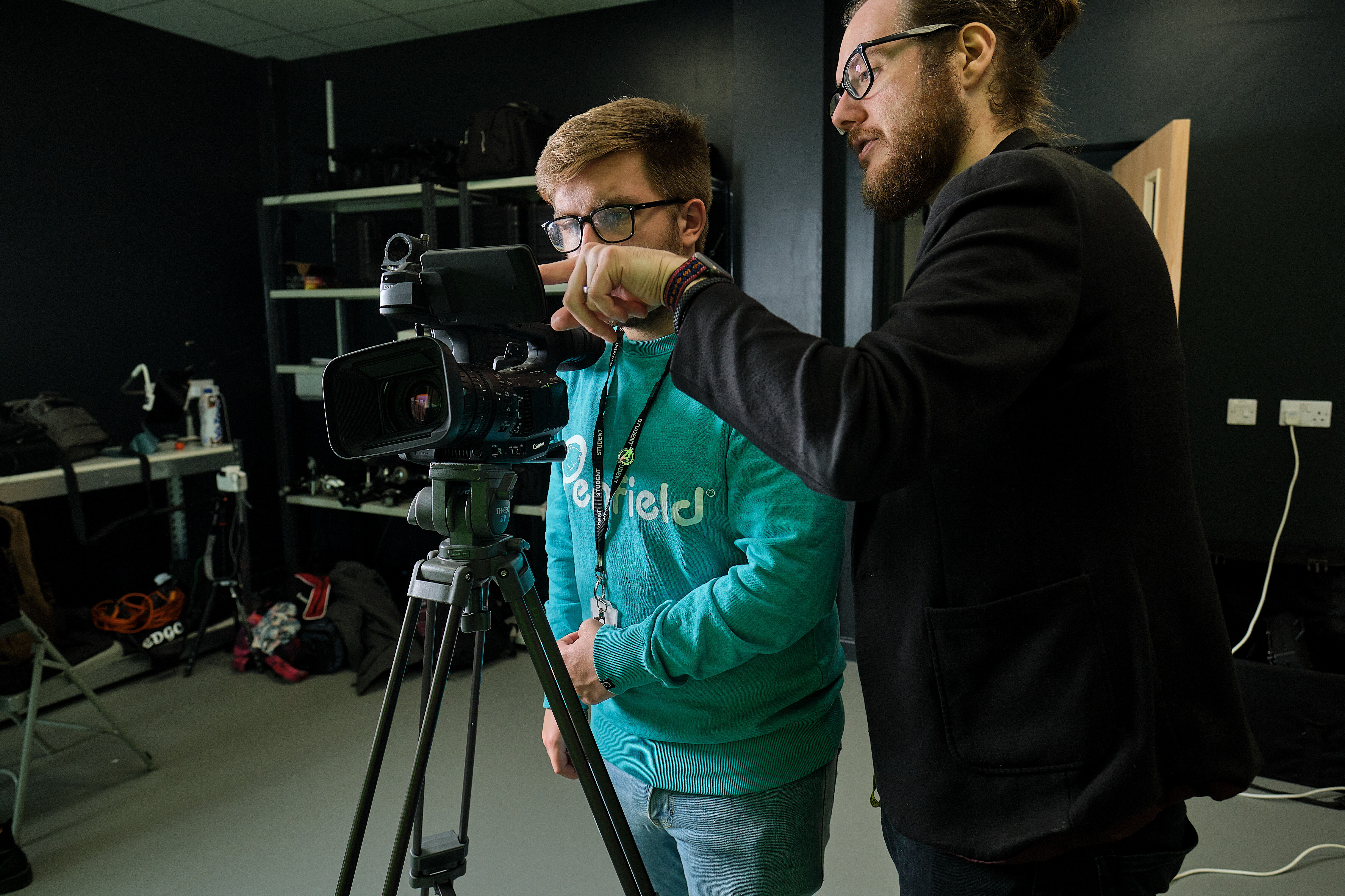 A lecturer standing next to a student looking through a camera.