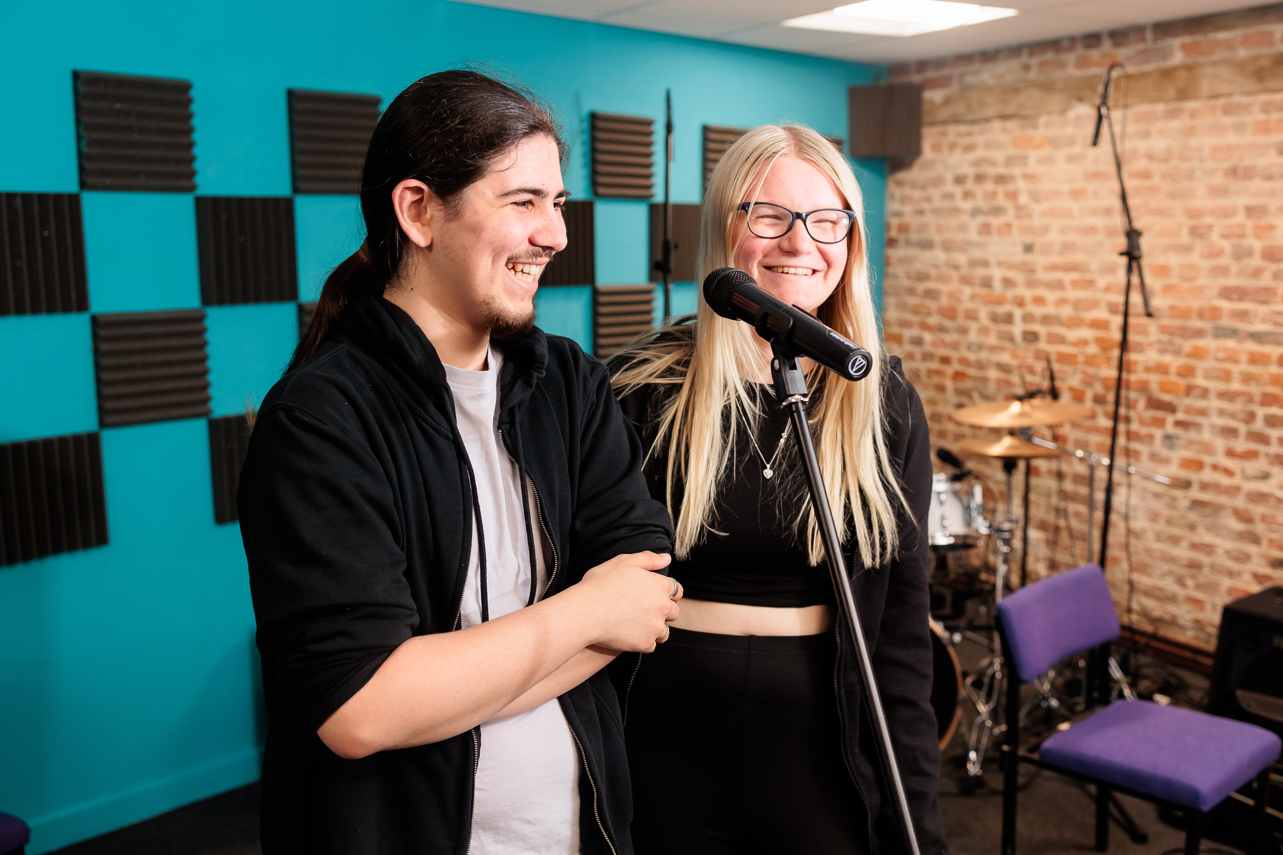 Two students stood at a microphone in a recording studio.