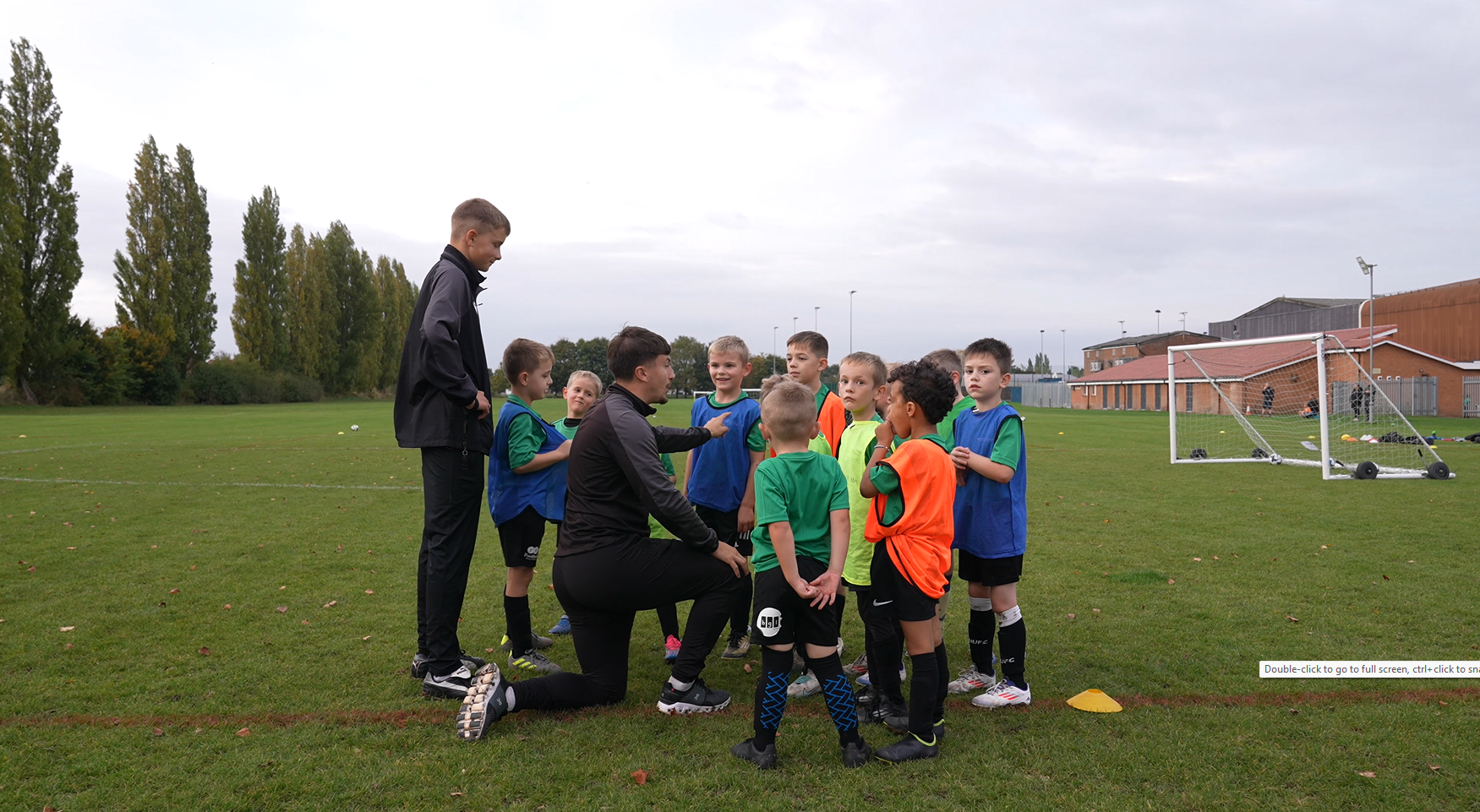 Students coaching a group of young children on a sports field.