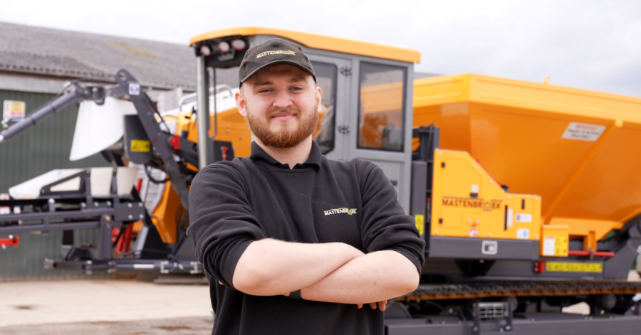A student stood with their arms folded in front of farmyard machinery.