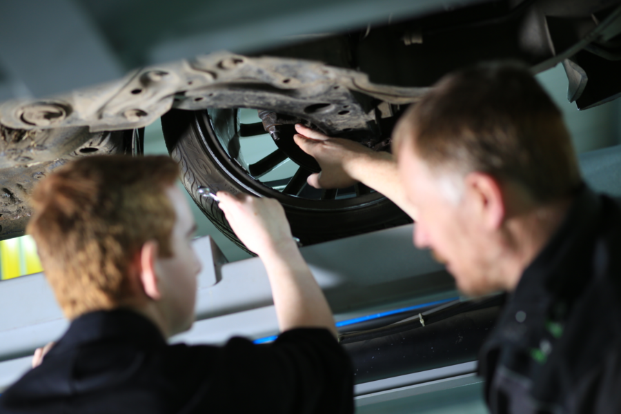 Two people inspecting a car tyre on a ramp.