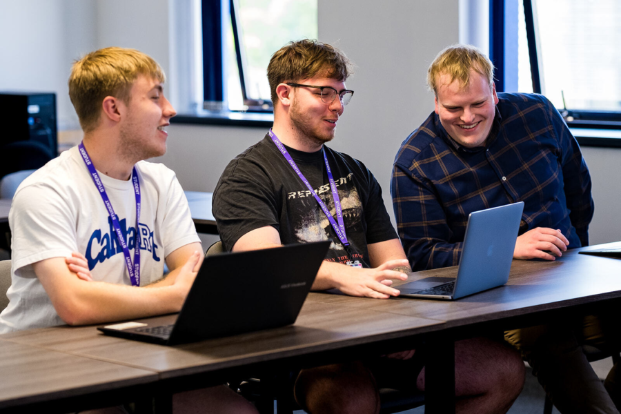 Three students on laptops discussing their work.