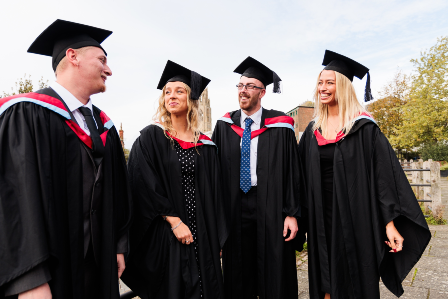 Students wearing graduation caps and gowns talking to each other.