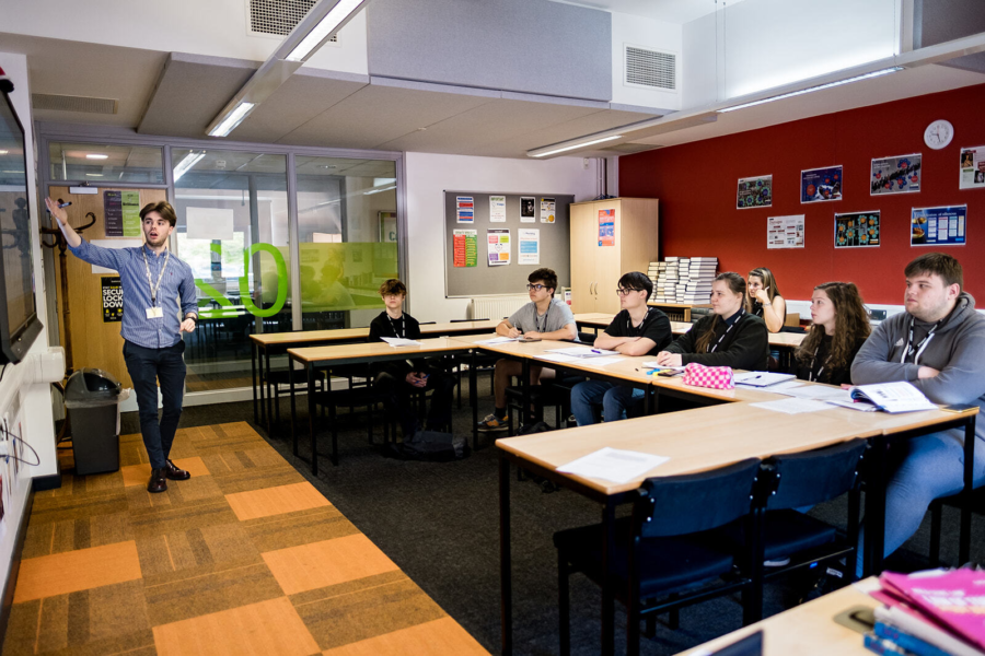 A lecturer pointing at a whiteboard whilst hosting a class.